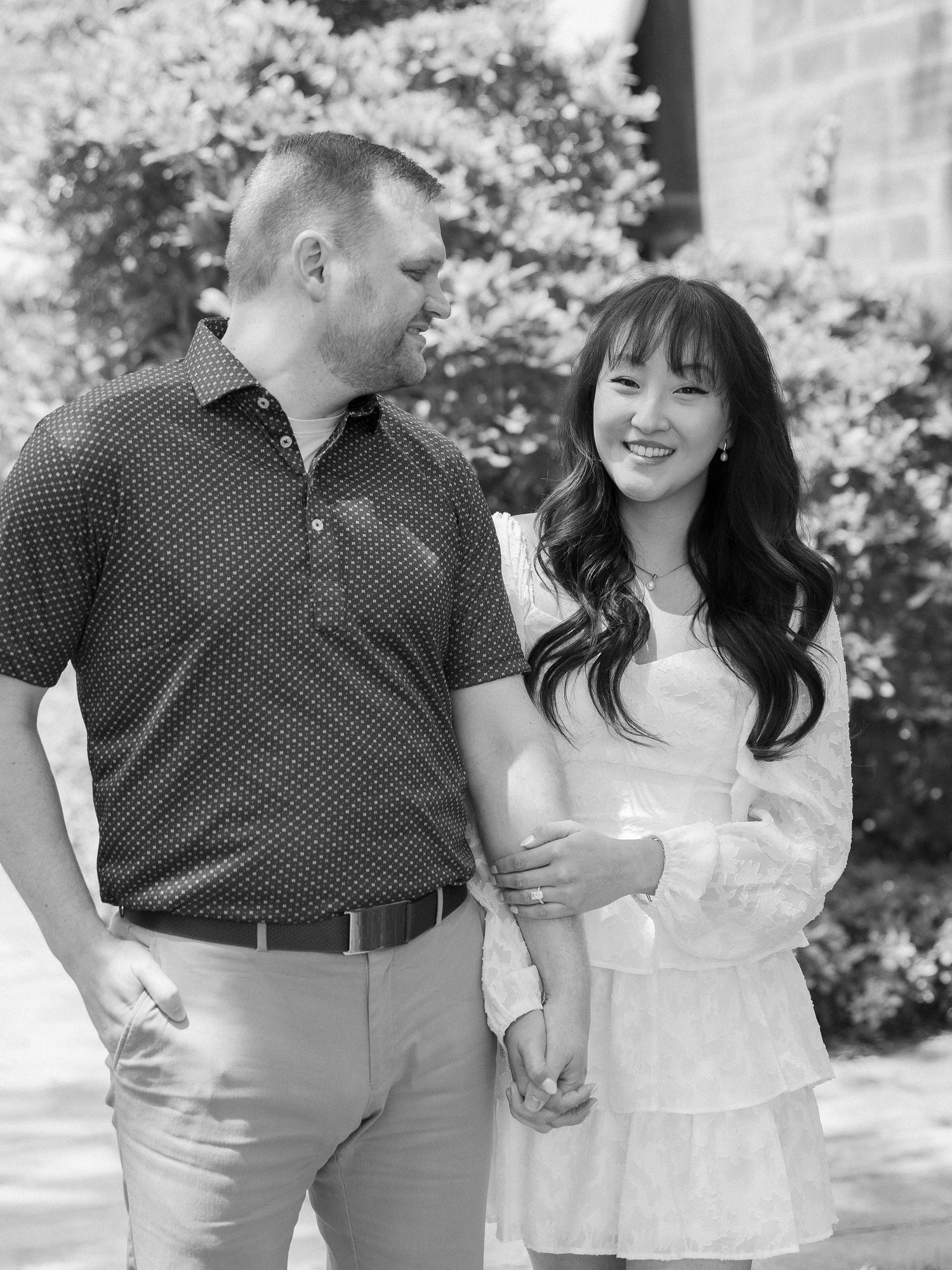 Romantic couple shares tender moments in a sunlit outdoor setting with white cherry blossoms in the background.