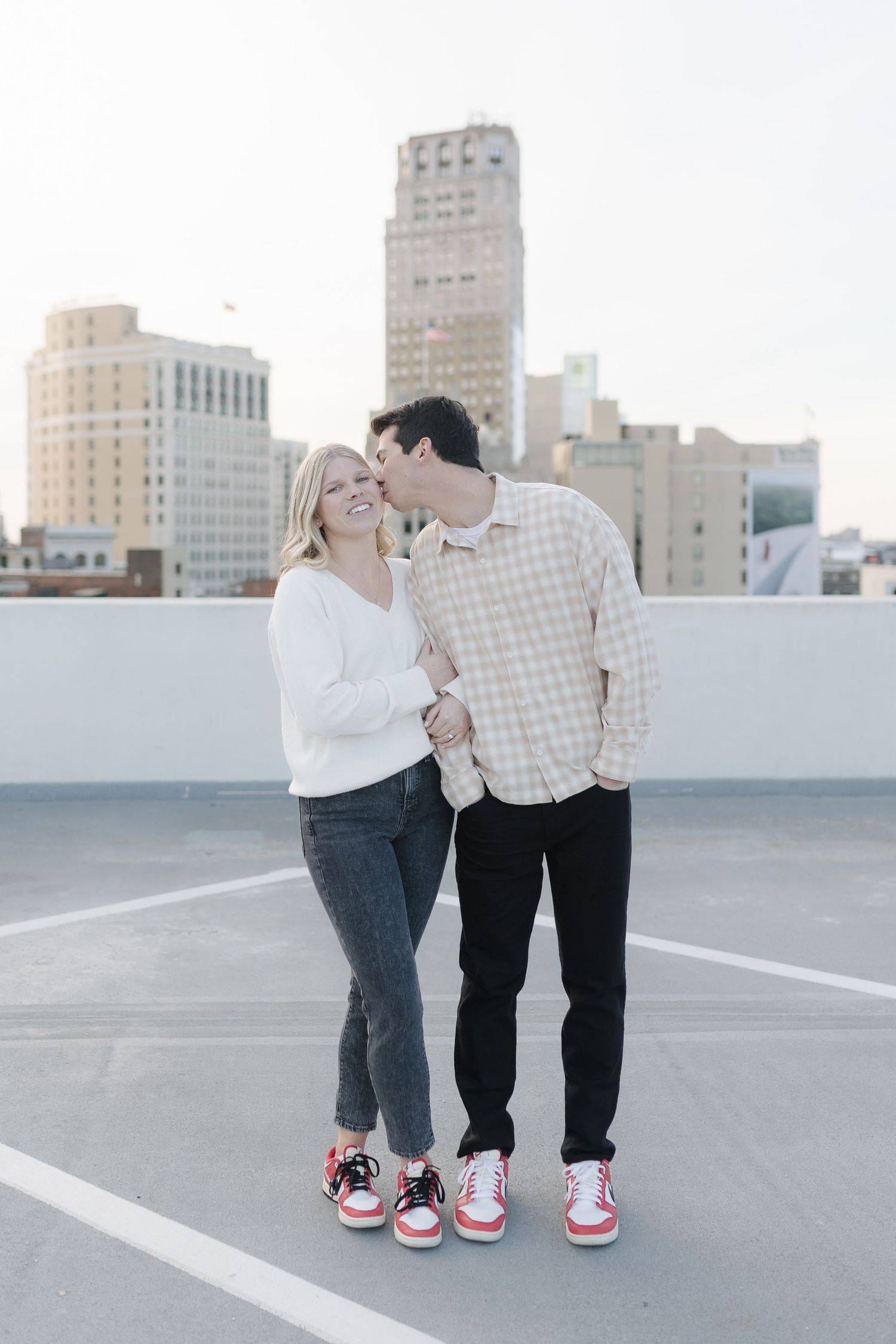 A couple in casual wear sharing a moment on a city rooftop with skyscrapers in the background.