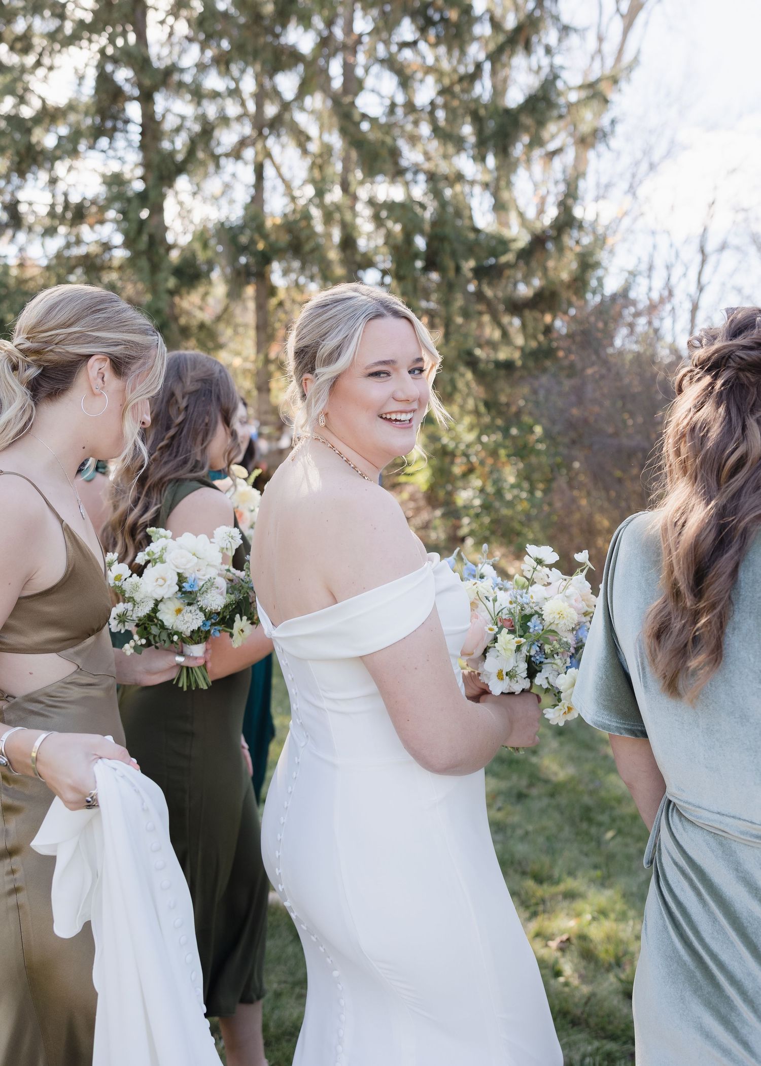 Bridesmaids in sage green dresses stand with a bride in white during an outdoor wedding celebration.