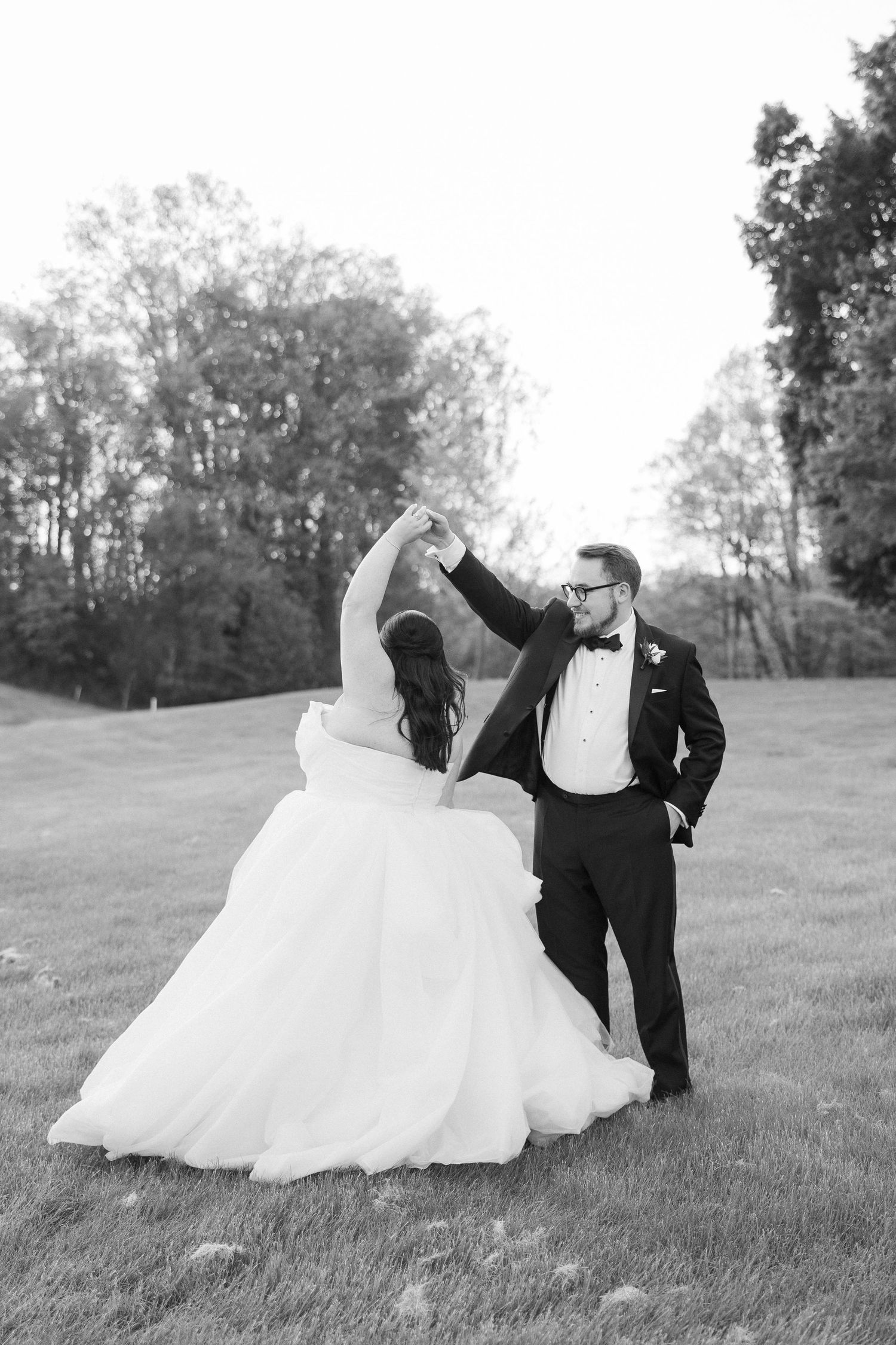 Wedding couple playfully posing on grassy hill in black and white photography.