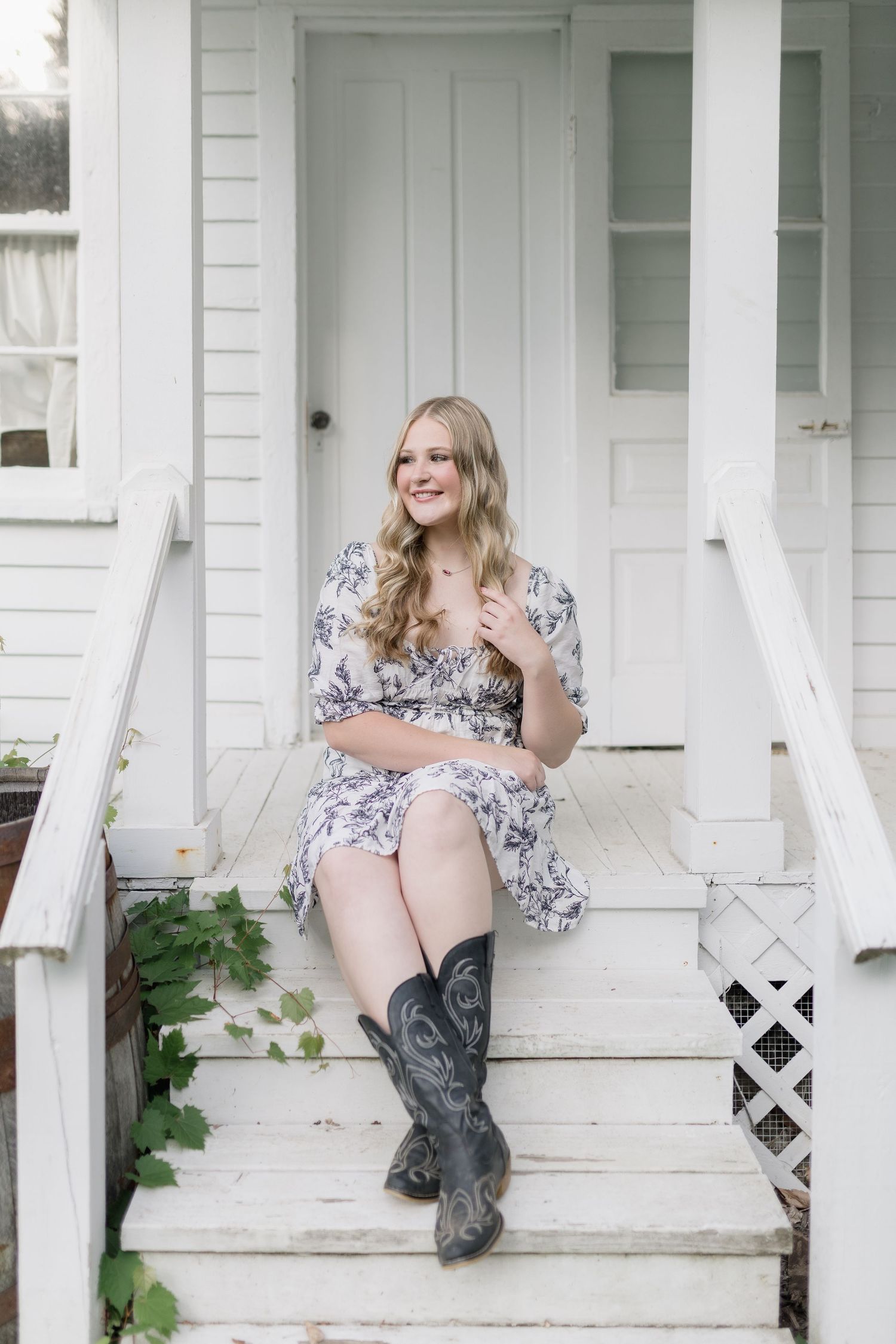 A floral dress and cowboy boots styled in a rustic photoshoot on white farmhouse porch steps.