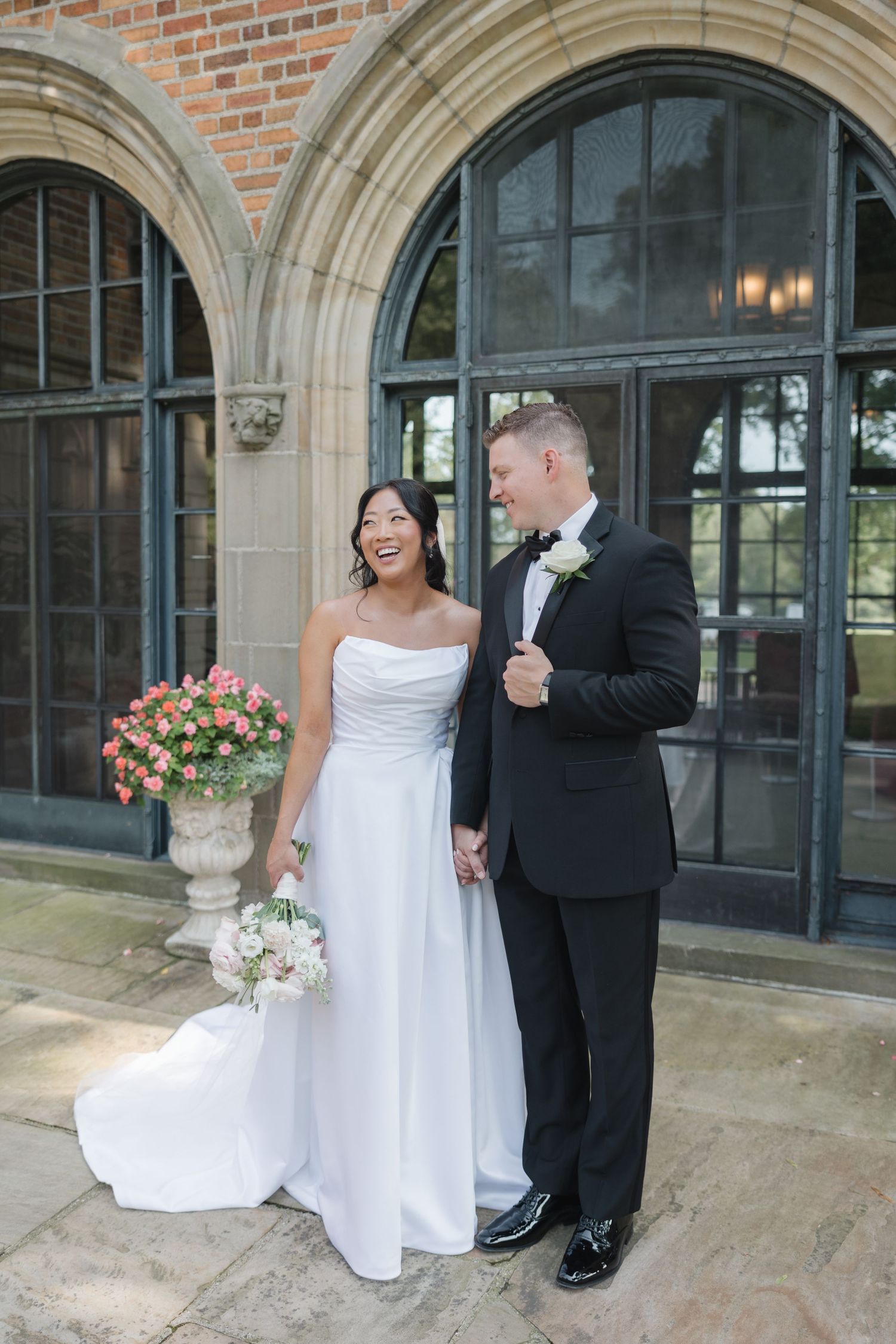 Couple sharing joyful moments outside historic brick building with arched windows.