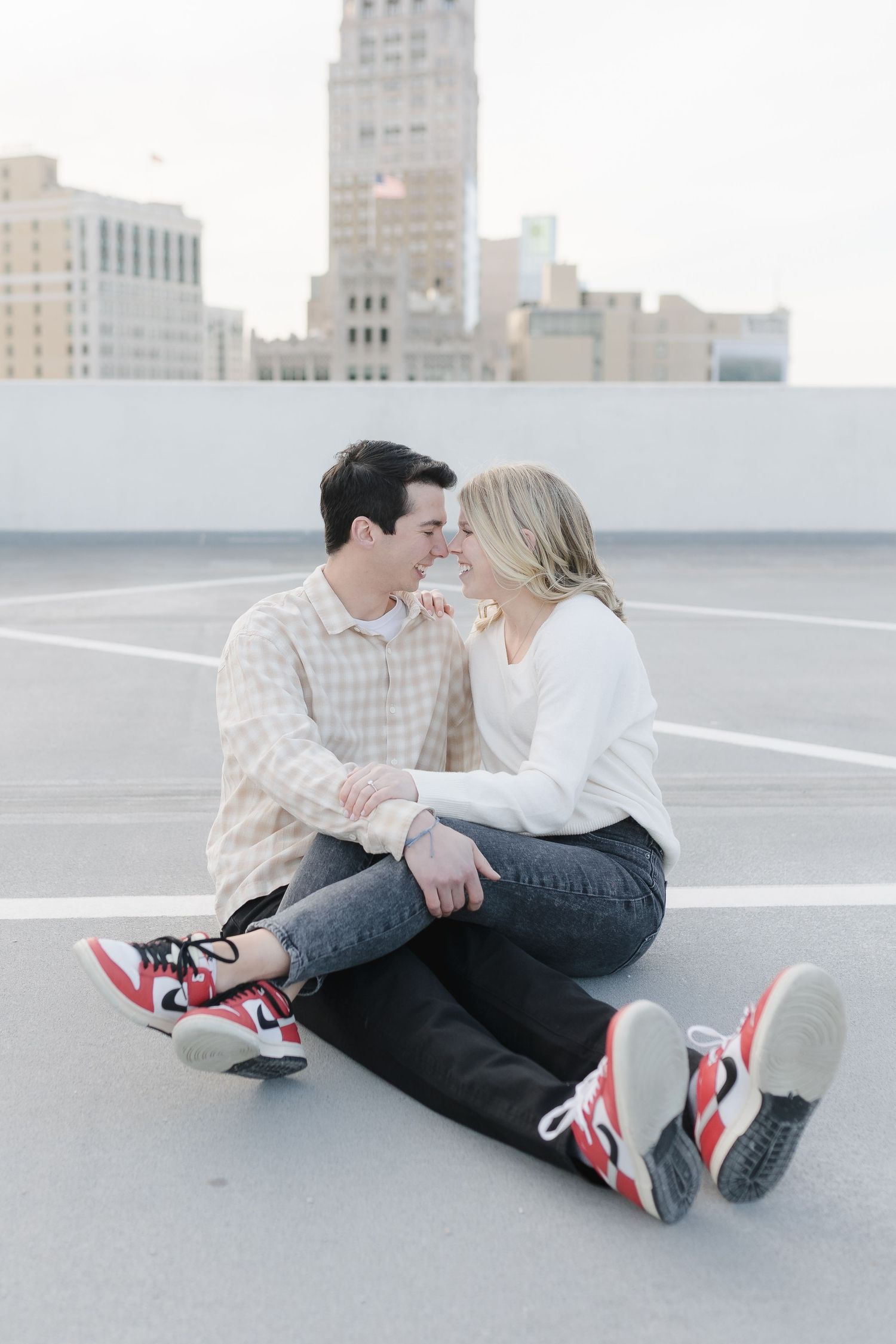A couple shares a tender moment while sitting on a rooftop with city buildings visible in the background.