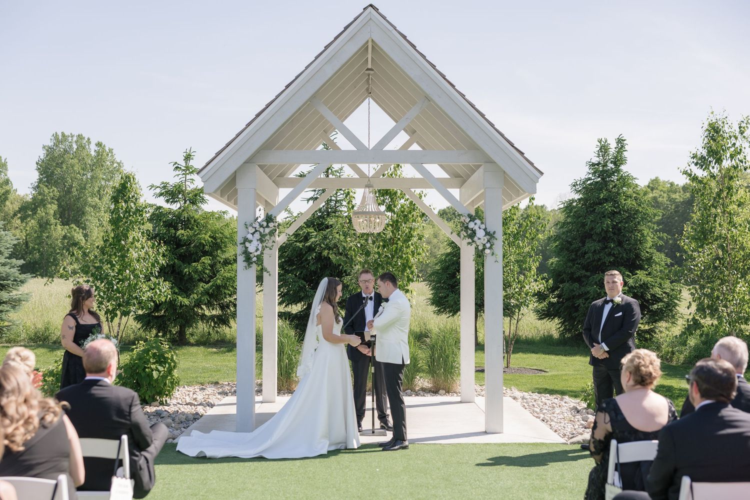 Bride and groom exchange vows under white gazebo at elegant outdoor wedding ceremony.