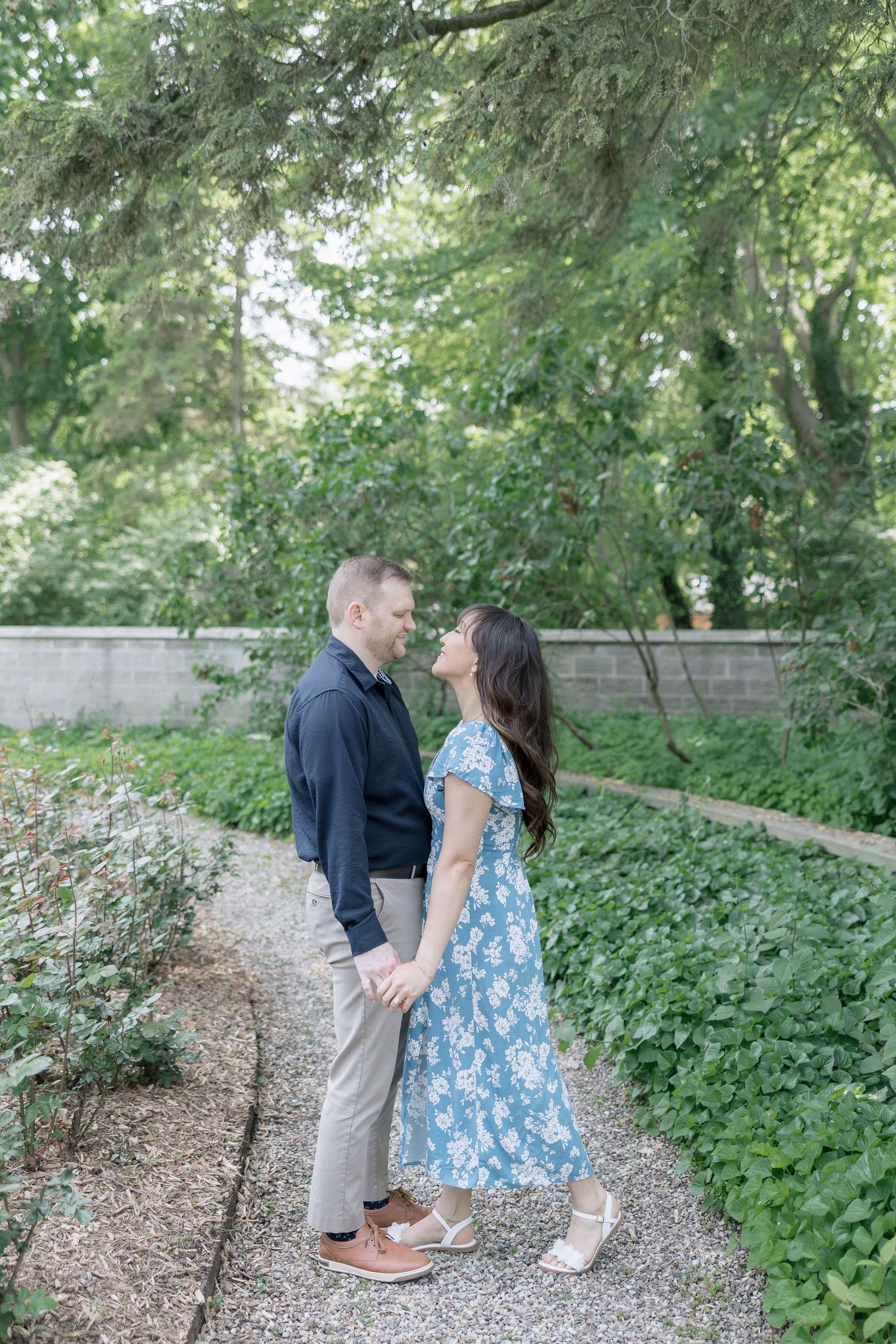 A couple shares intimate moments while walking along a garden path surrounded by lush greenery.