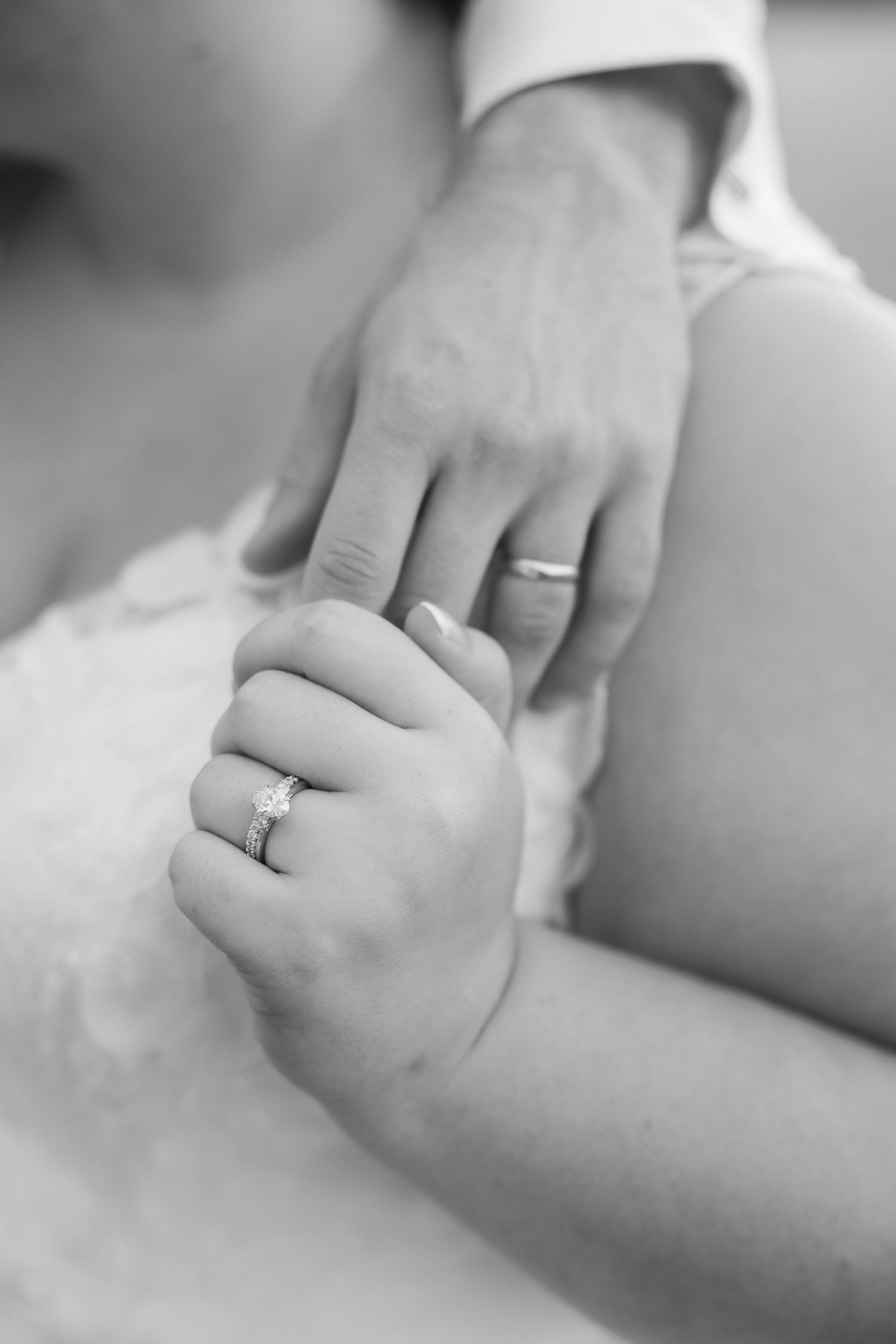 Close-up black and white photo of wedding rings and clasped hands showing newlywed details.