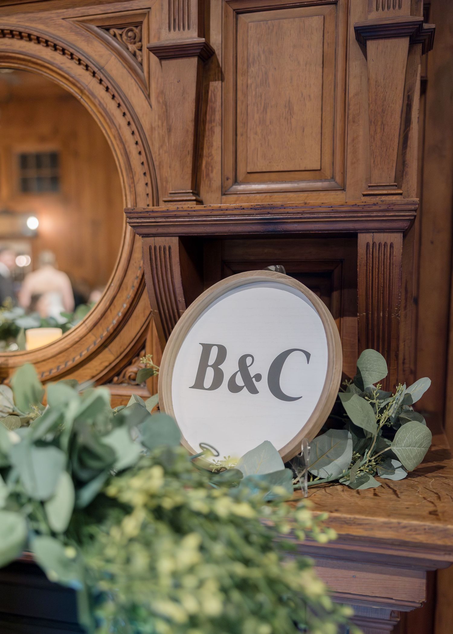 Wedding monogram sign with B&C letters surrounded by eucalyptus leaves on wooden display.