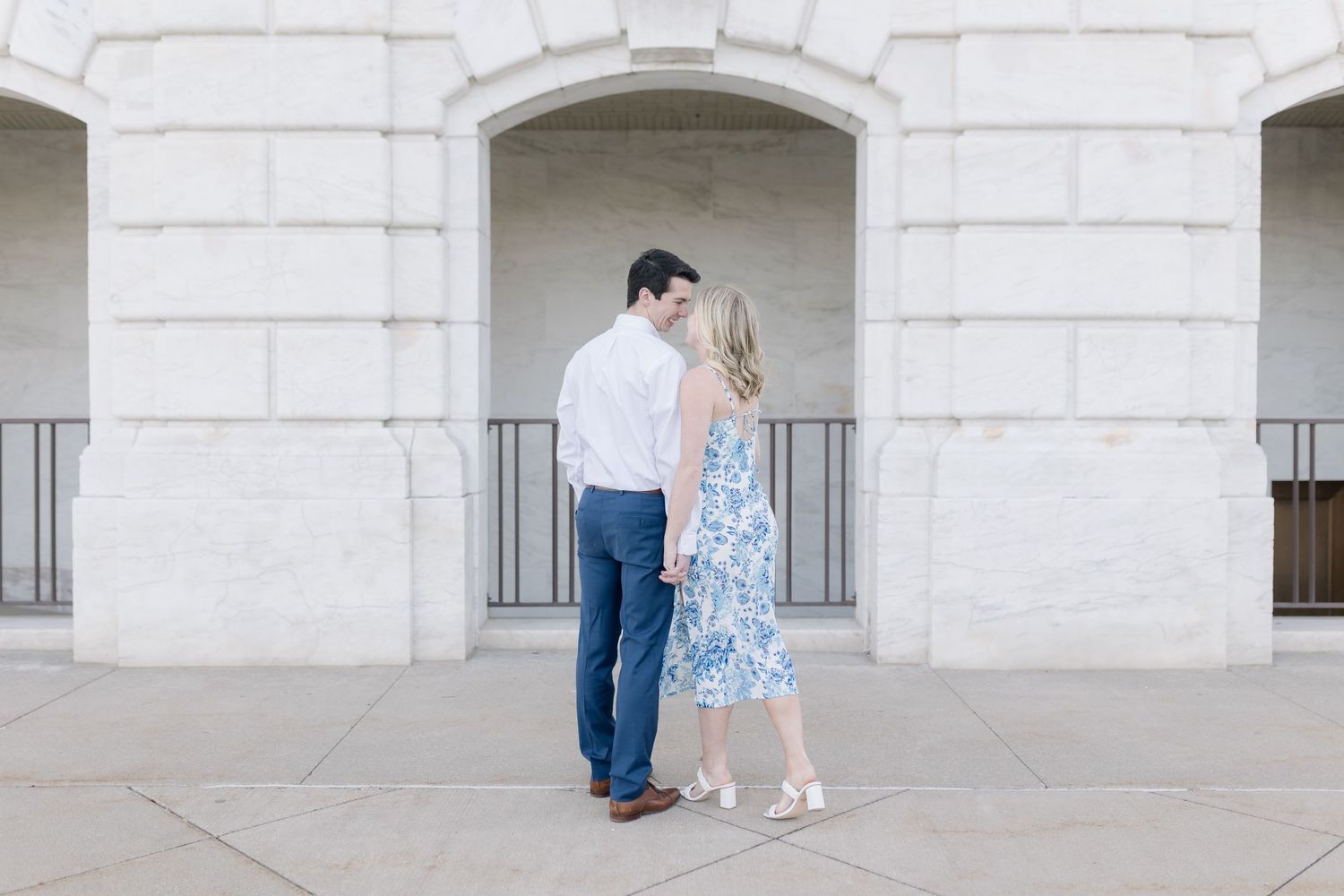 A couple in elegant attire shares an intimate moment under a white stone archway.