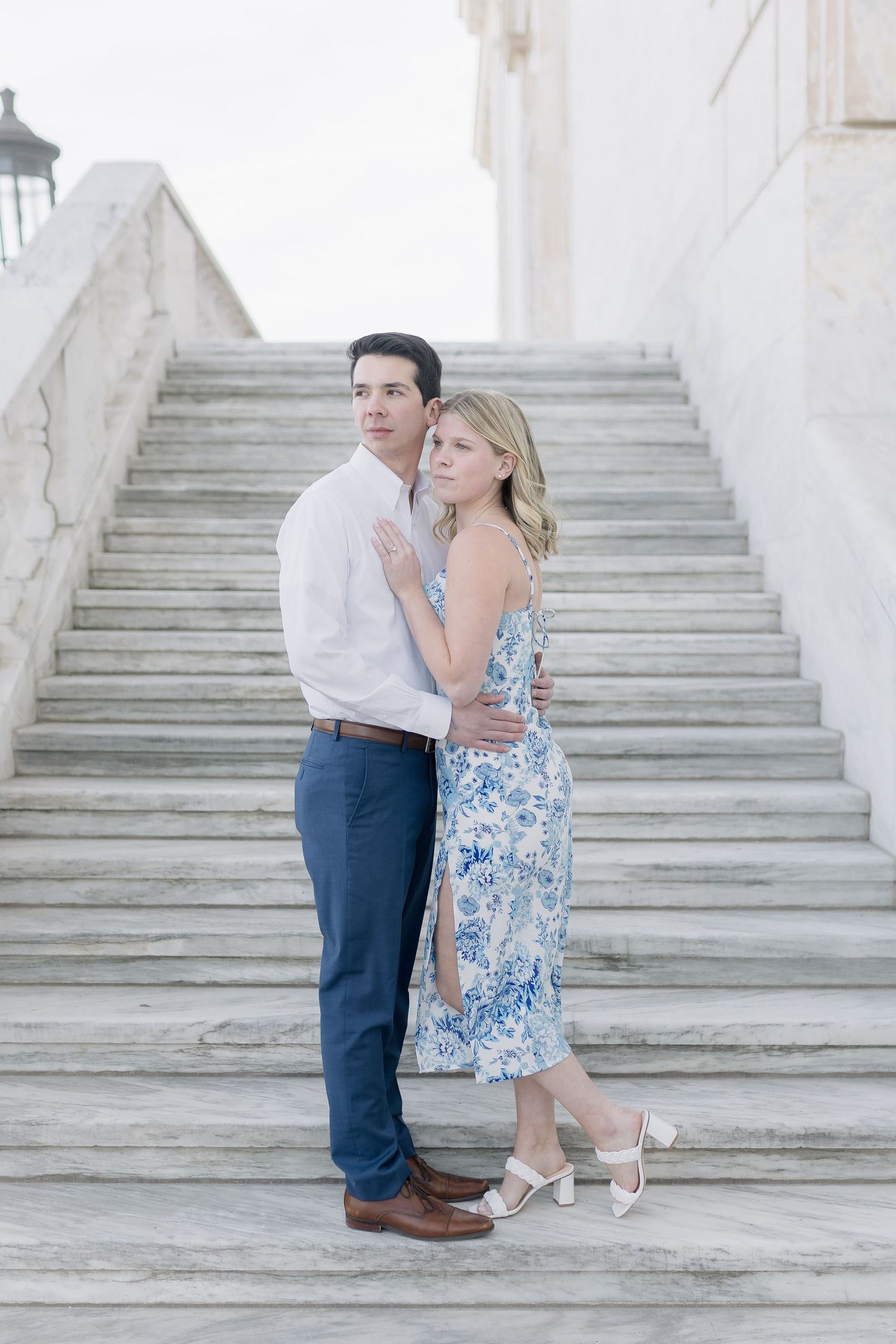 A romantic couple posing on elegant white marble stairs with classic architecture in the background.