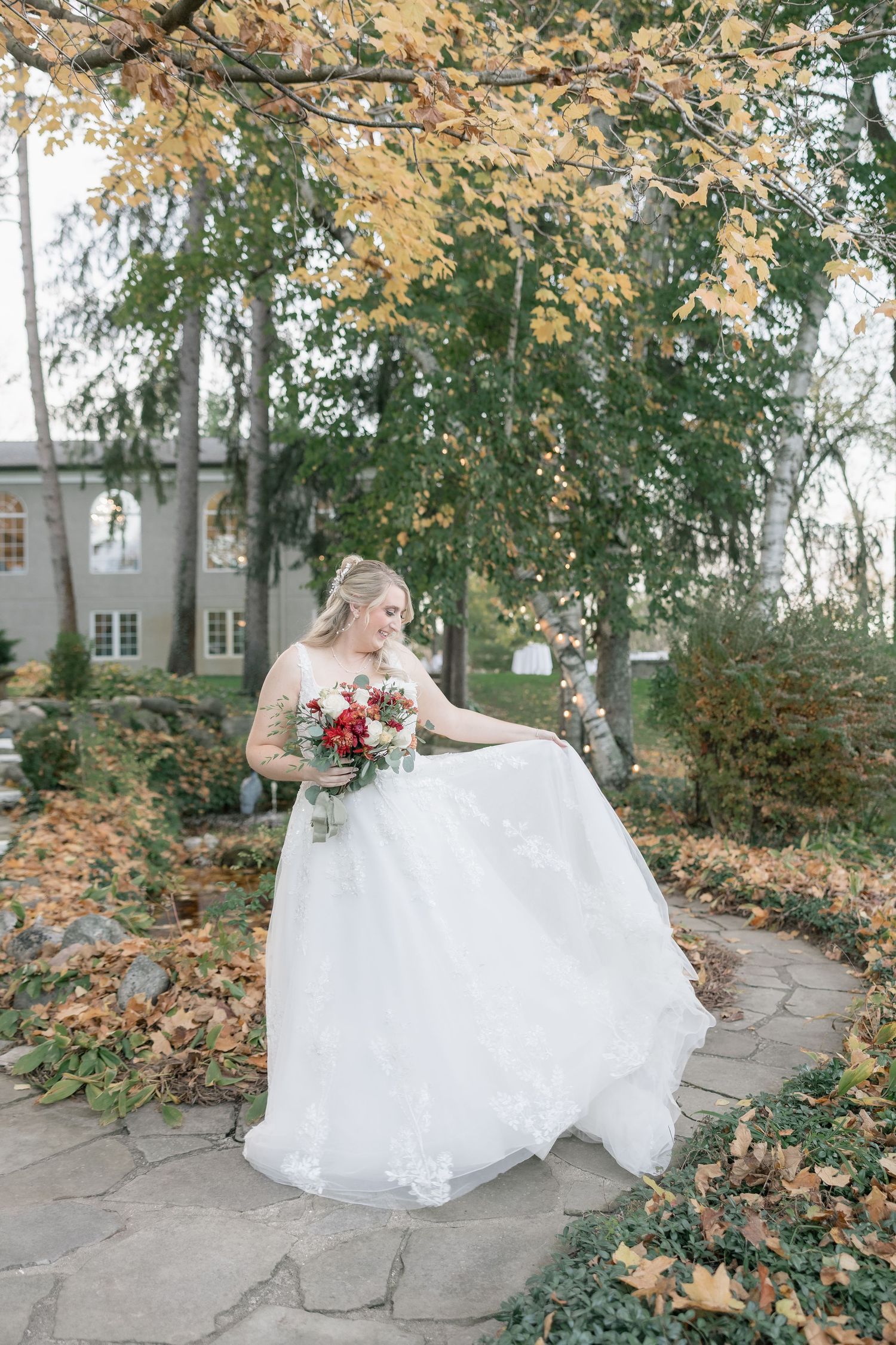 A bride in a white ballgown twirls among autumn leaves on a stone pathway during a fall wedding photoshoot.