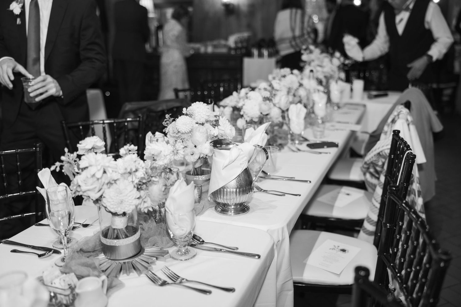 Black and white photo of an elegant wedding reception table setting with floral centerpieces.