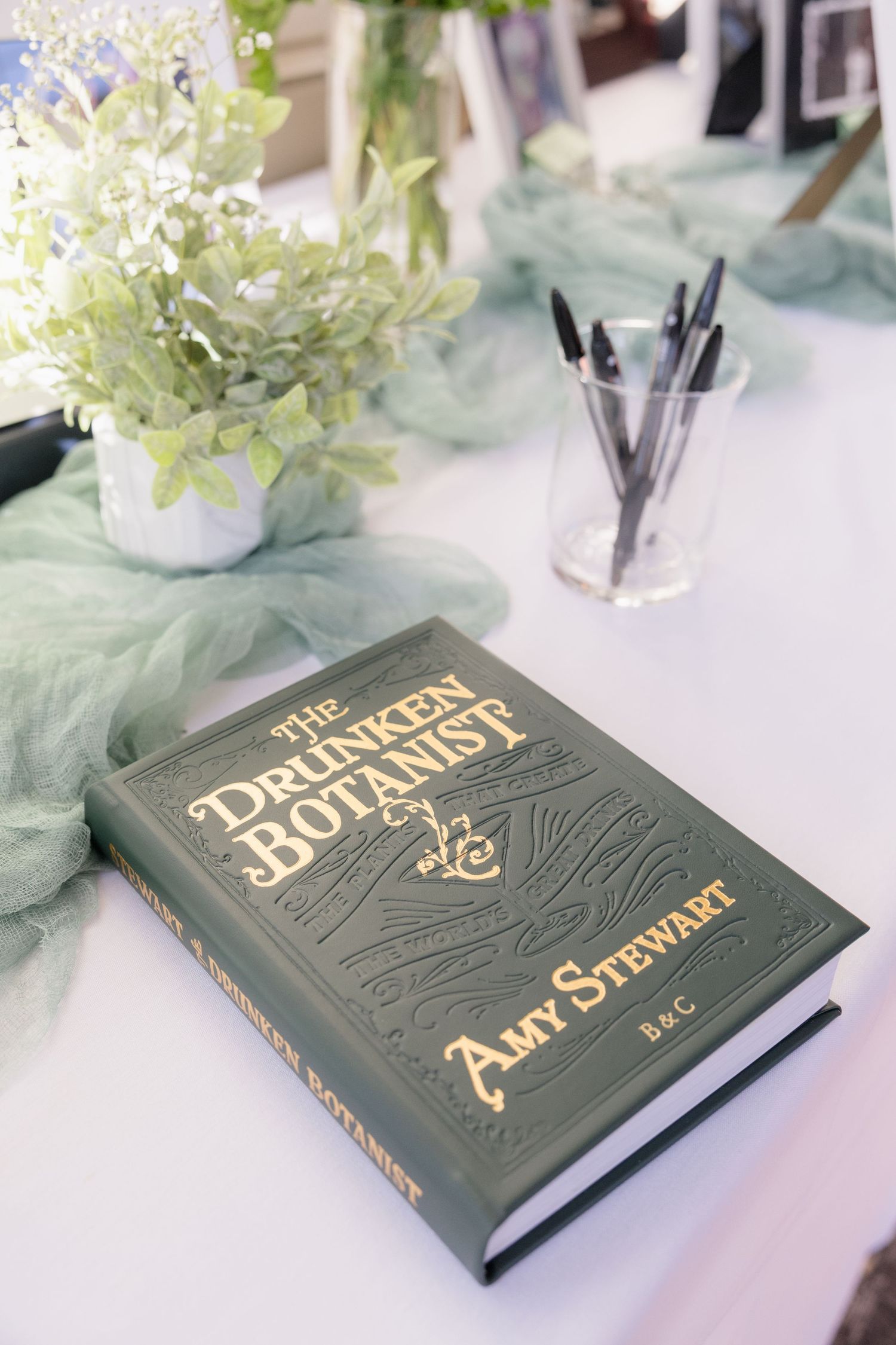 The Drunken Botanist book on white table with green decor and white hydrangeas.