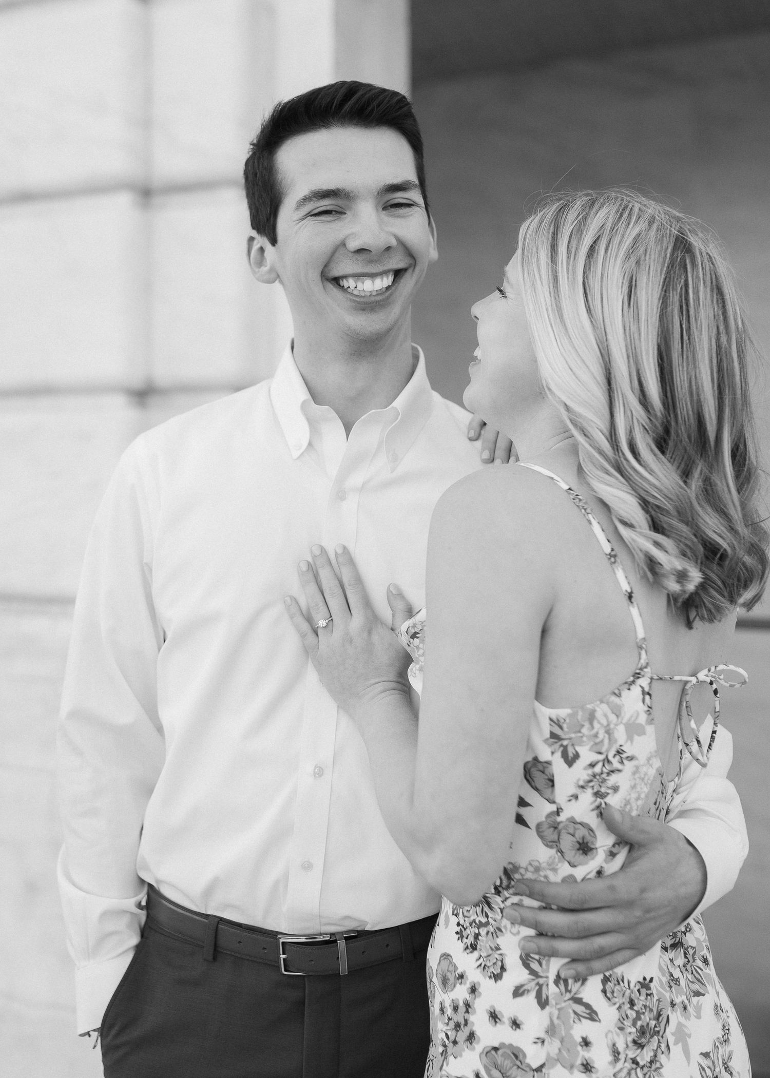 A couple shares a joyful moment in black and white photography against a stone backdrop.