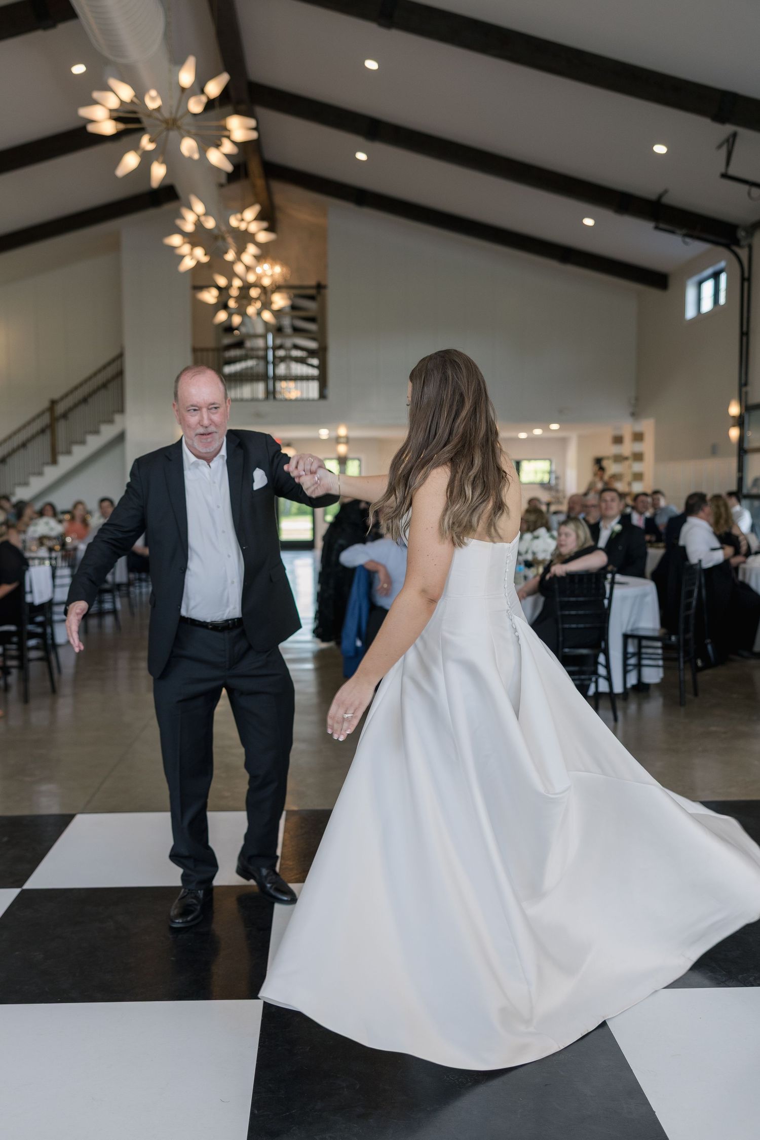 Bride dances with father on black and white checkered dance floor at wedding reception.