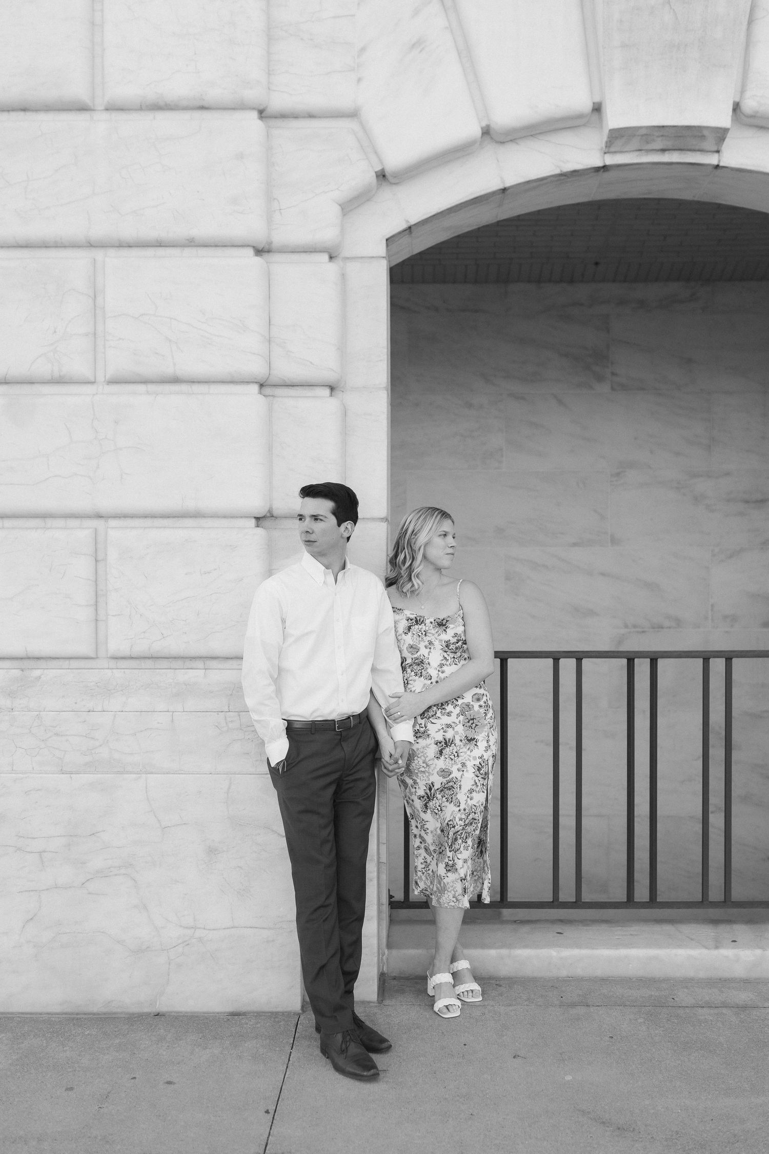 A romantic couple shares playful moments against a white stone building with arched windows.