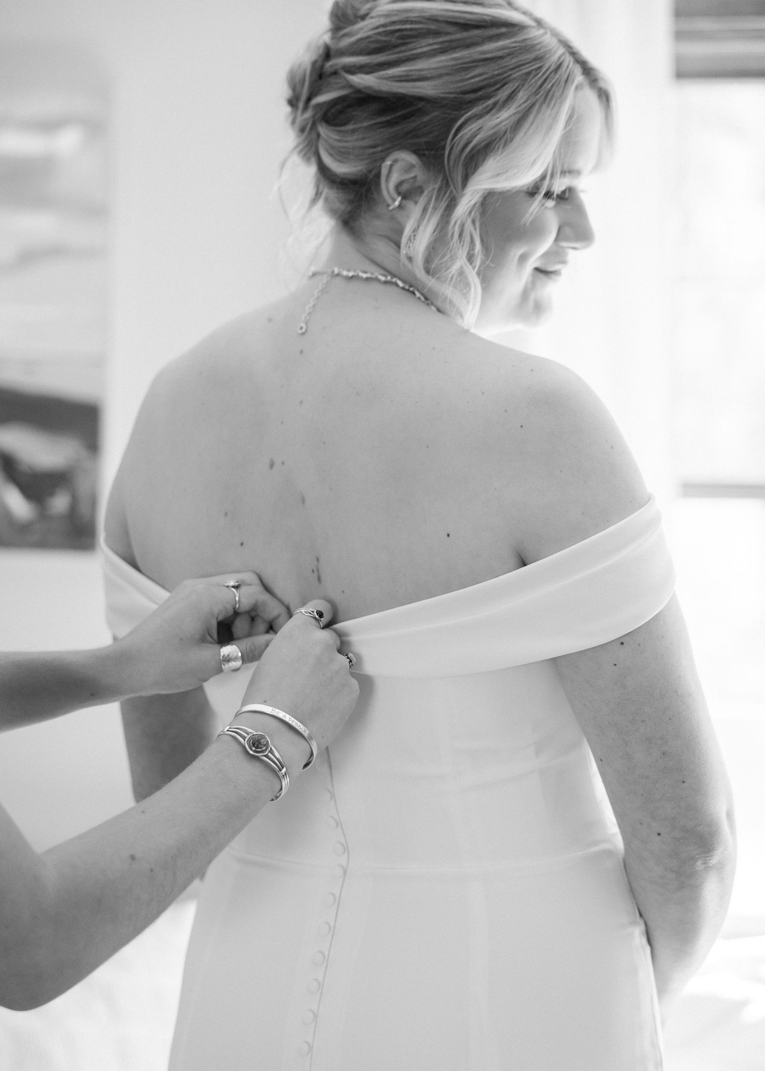 Close-up view of a white wedding dress being buttoned up from behind.