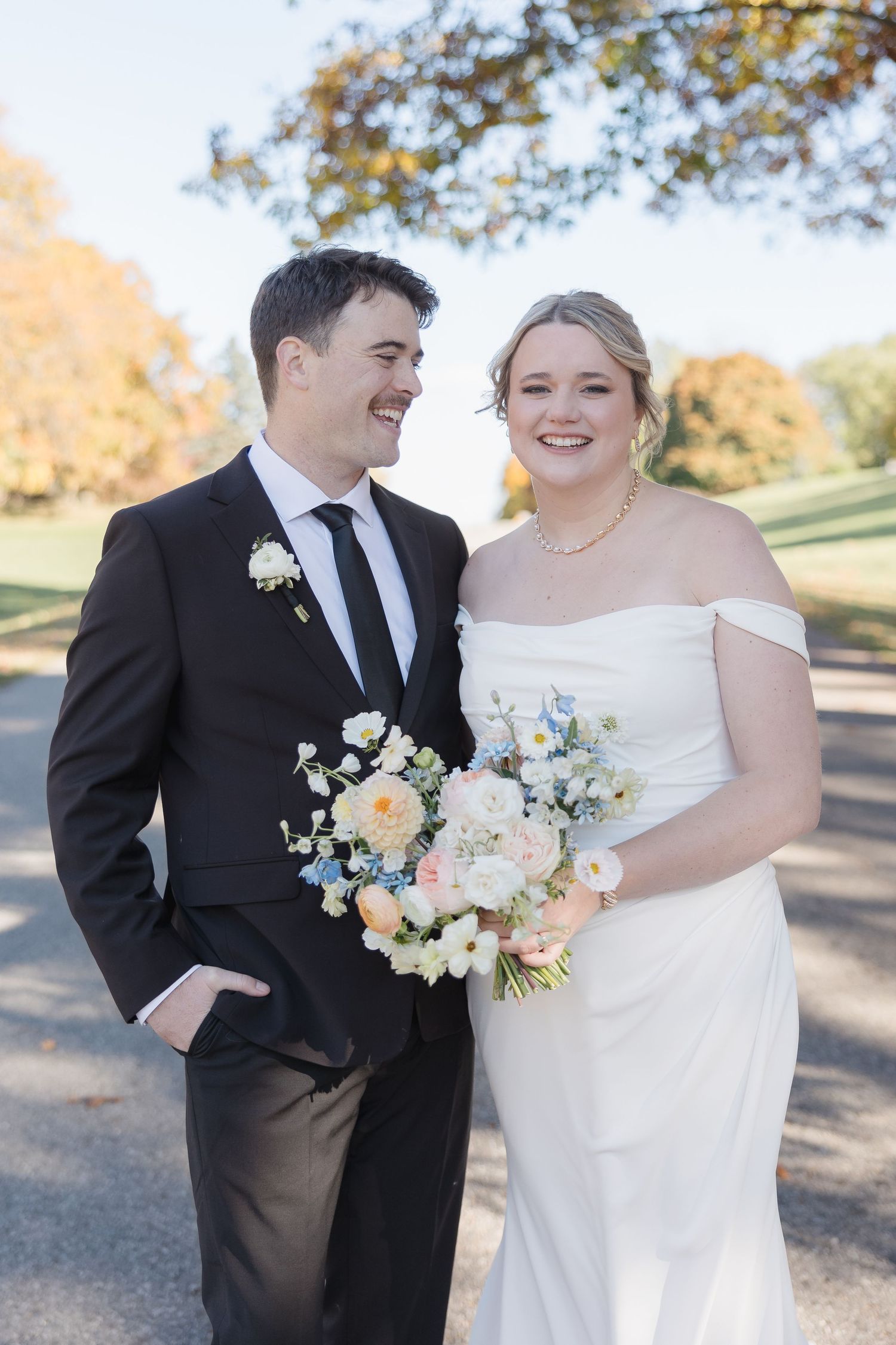 Happy newlyweds pose together with colorful pastel bouquet on sunny autumn path.