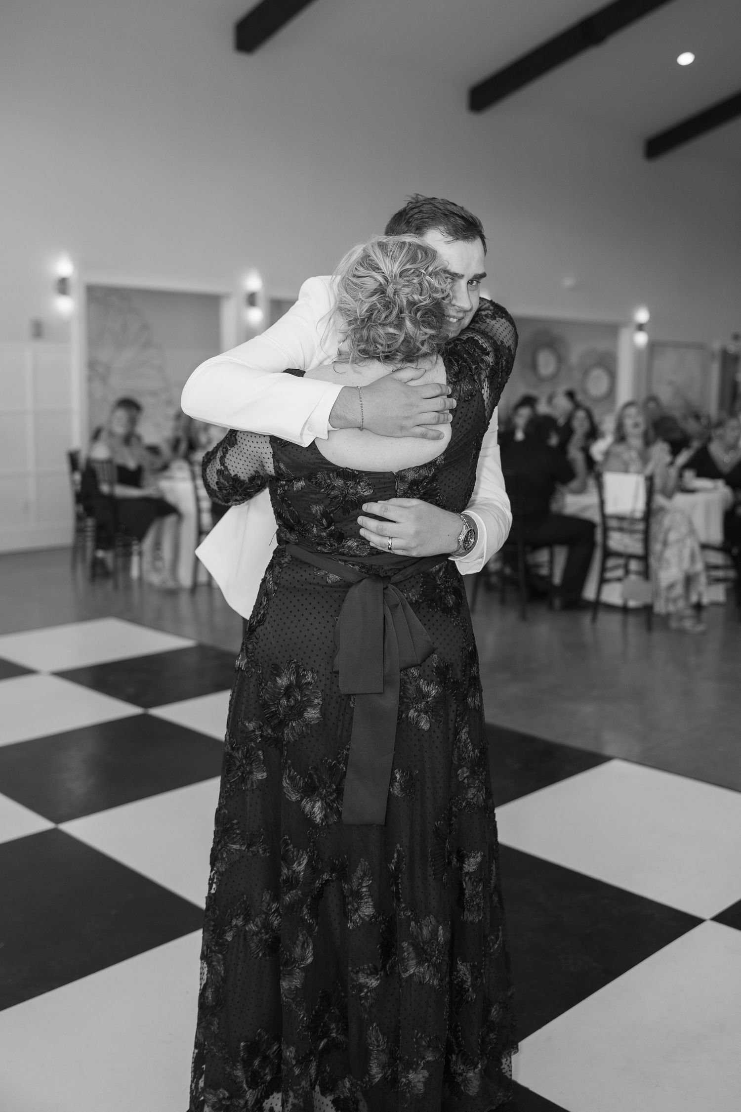 Black and white photo of a groom and his mother sharing an emotional hug during the mother-son dance at a wedding reception.