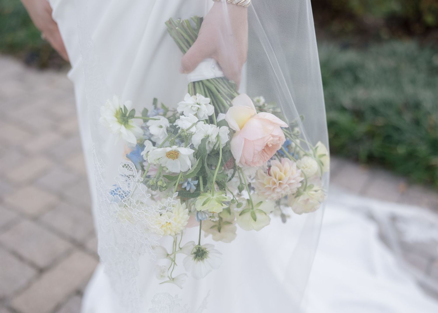 Close-up of a delicate pastel wedding bouquet with pink and blue flowers behind sheer veil fabric.