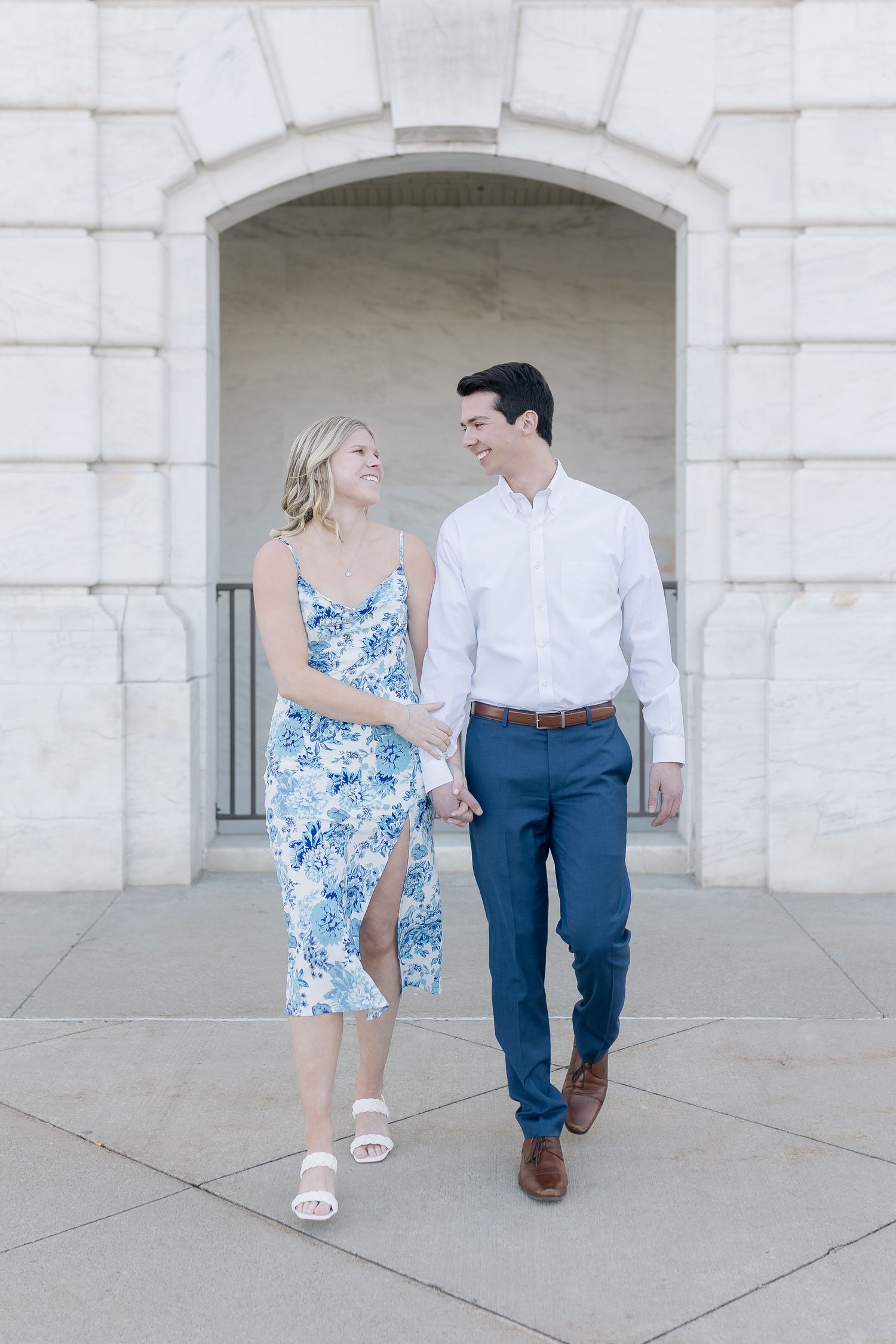 Couple in coordinated blue and white outfits walking together under an elegant stone archway. Detroit Michigan Art Institute.