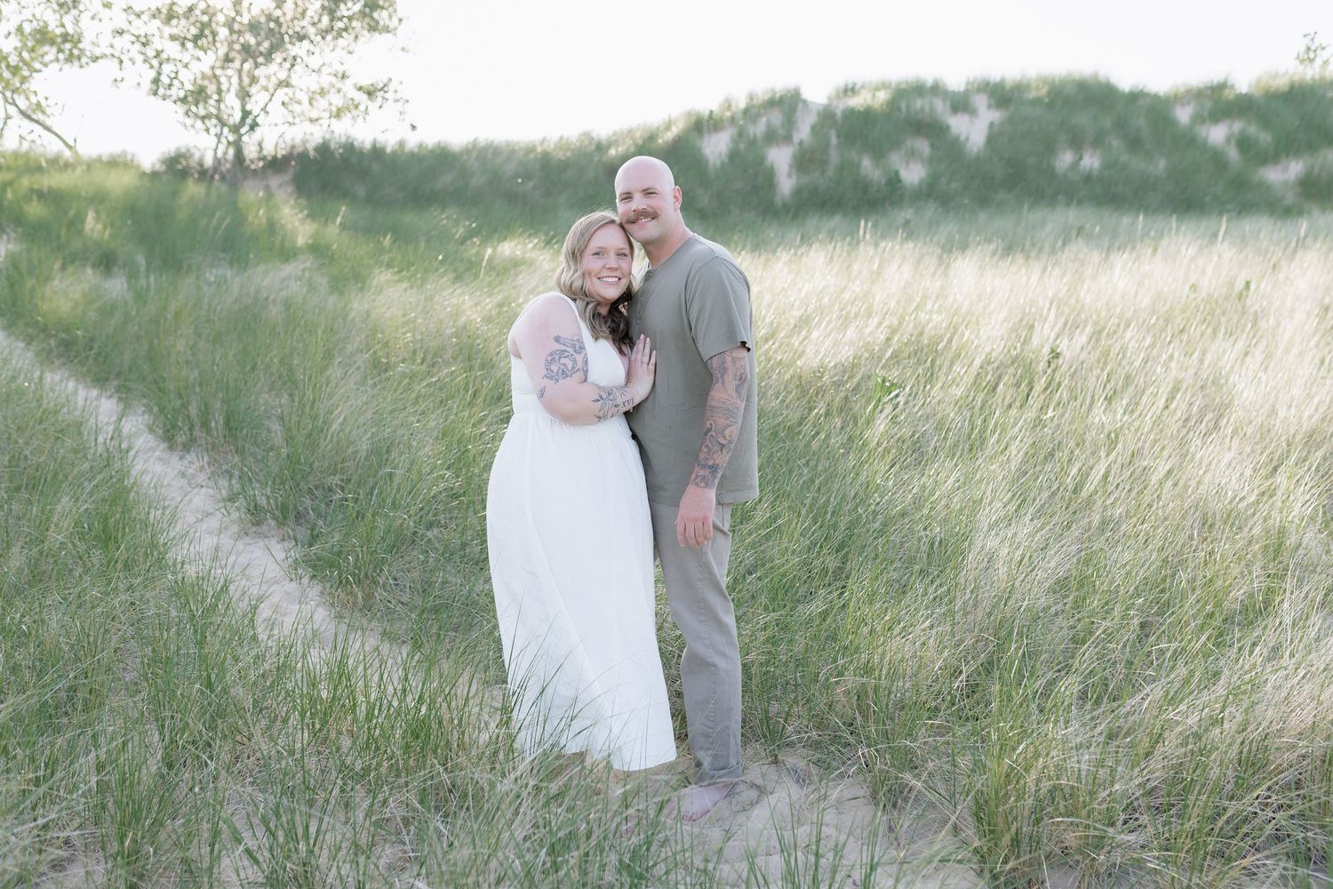 A couple embraces in a sunlit meadow with tall grass swaying in the summer breeze.