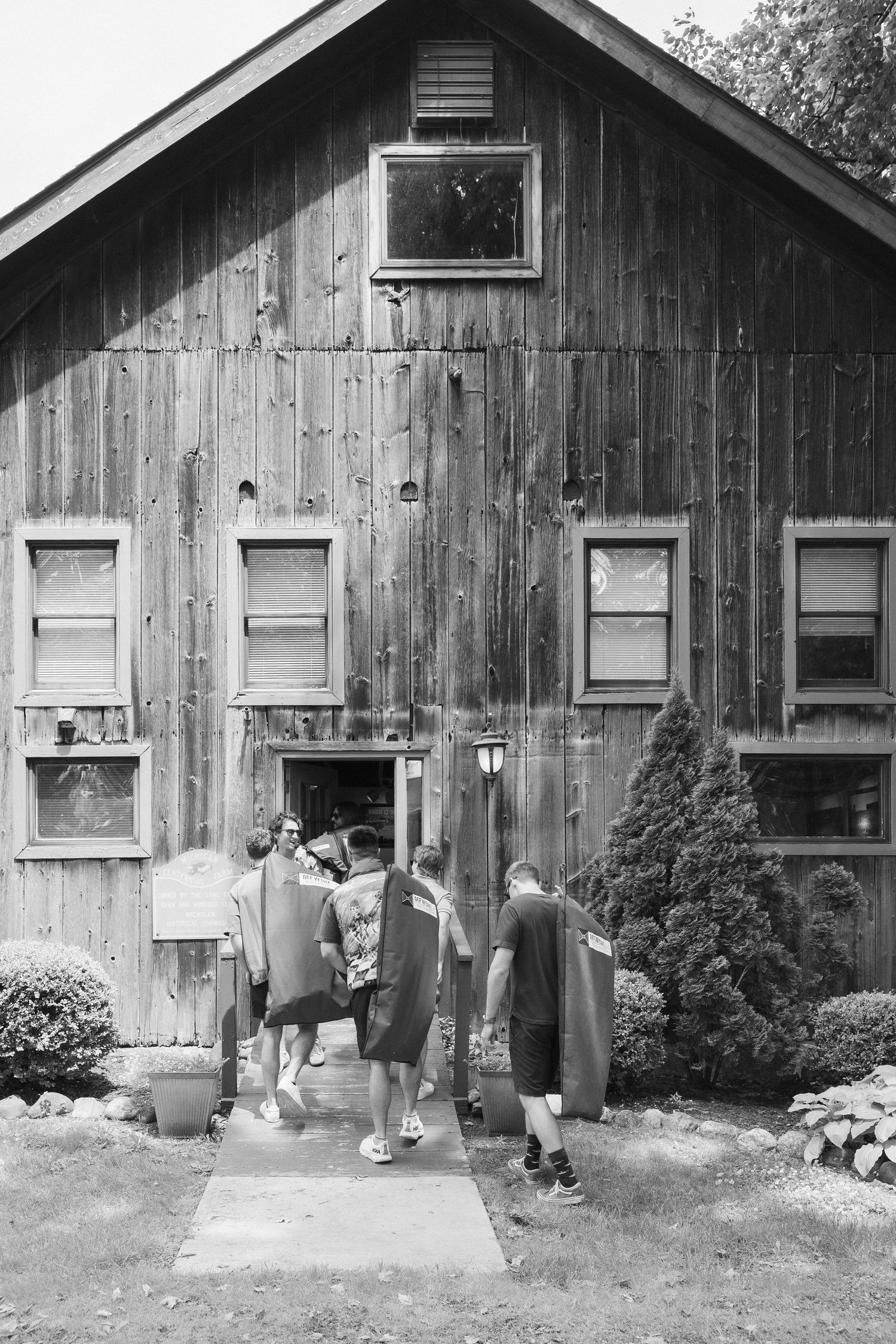 A series of four black and white photos showing people walking past a rustic wooden cabin with white-trimmed windows.