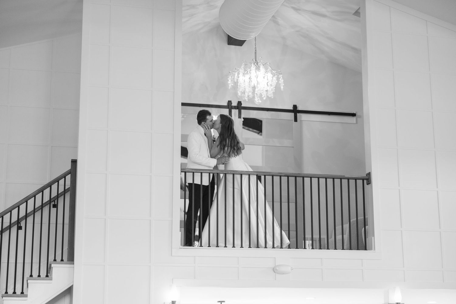 Black and white photo of bride and groom sharing a romantic moment on a balcony with chandelier.