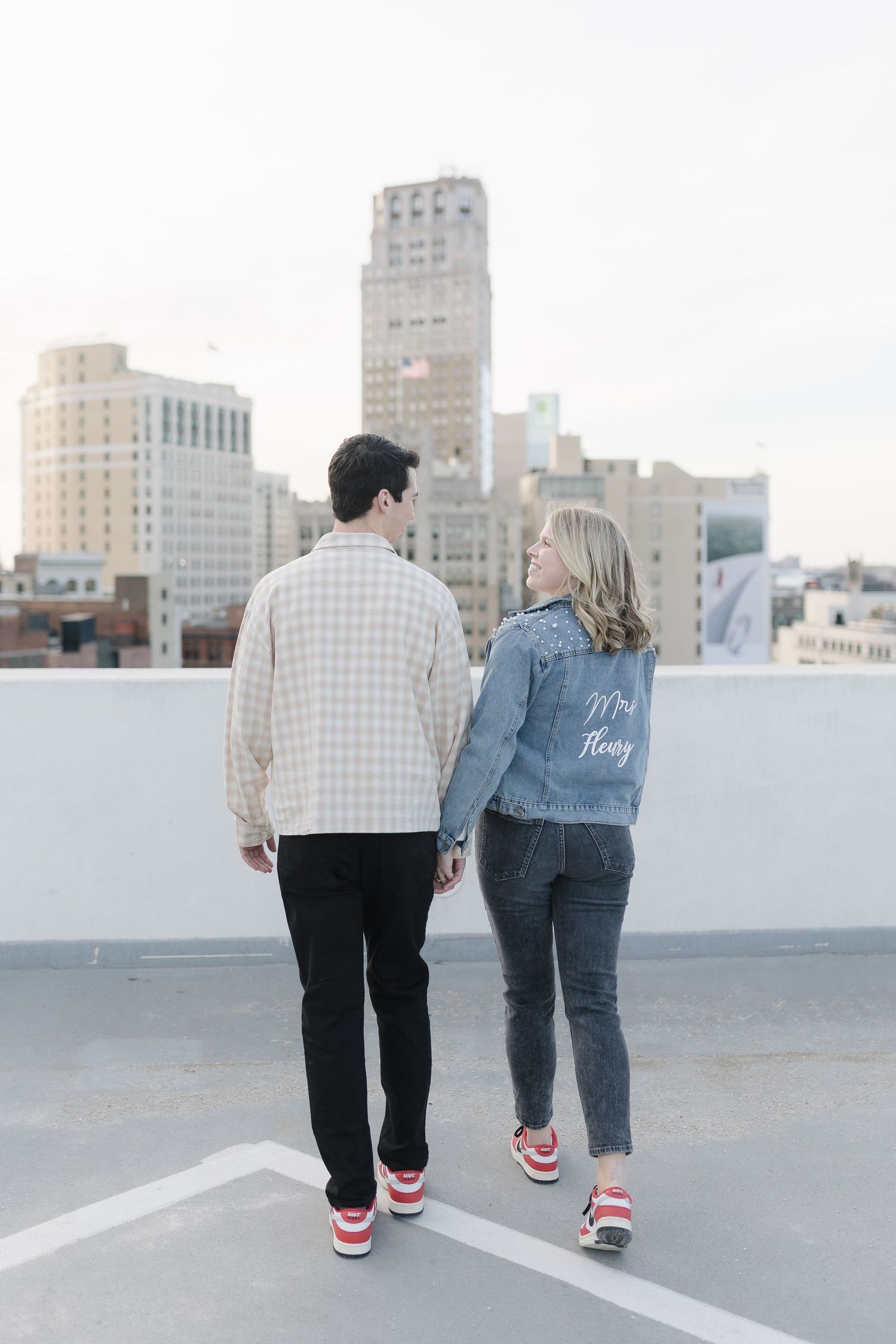 Couple wearing matching sneakers standing on rooftop overlooking city skyline.