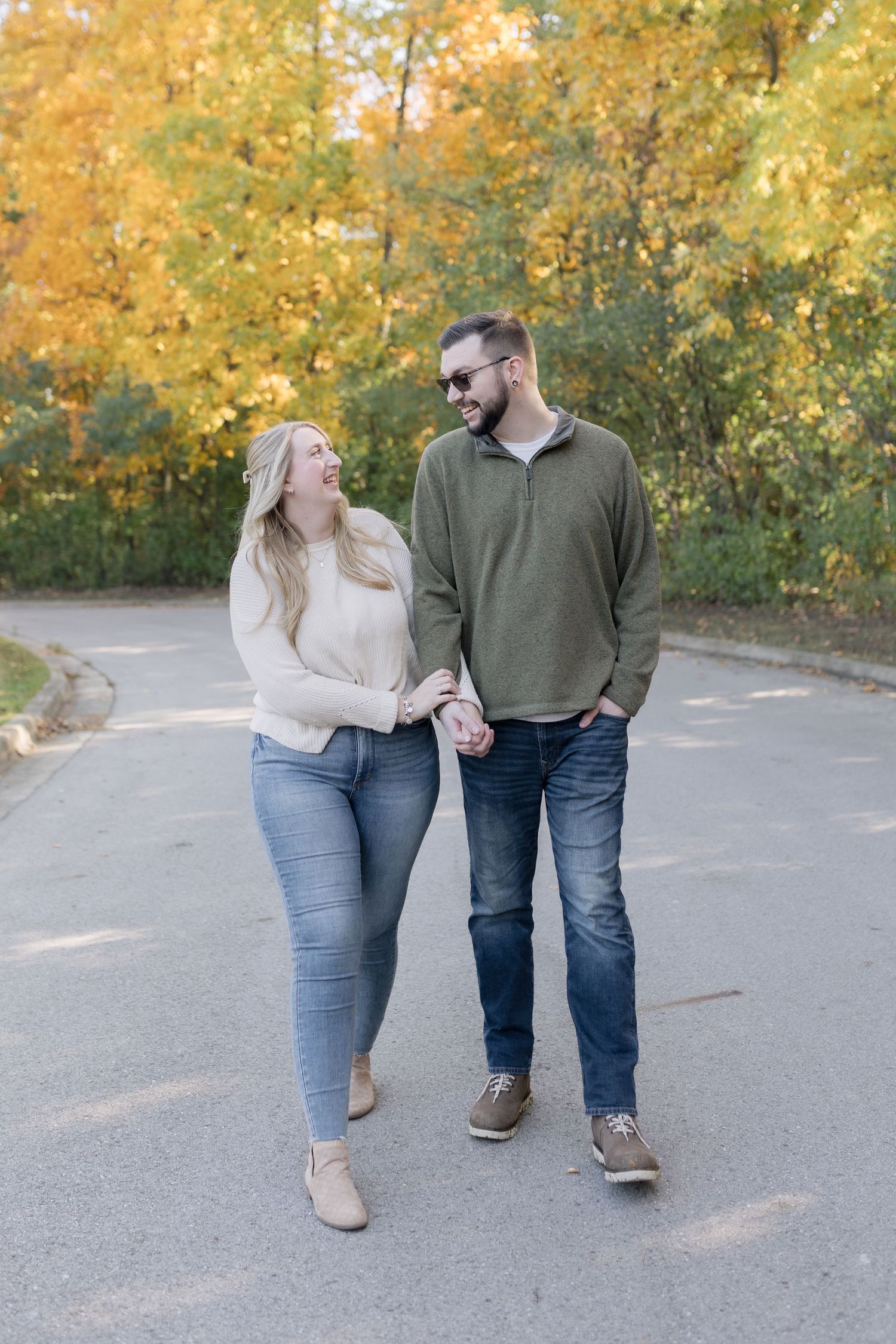 Couple walking hand in hand on path surrounded by golden autumn foliage.