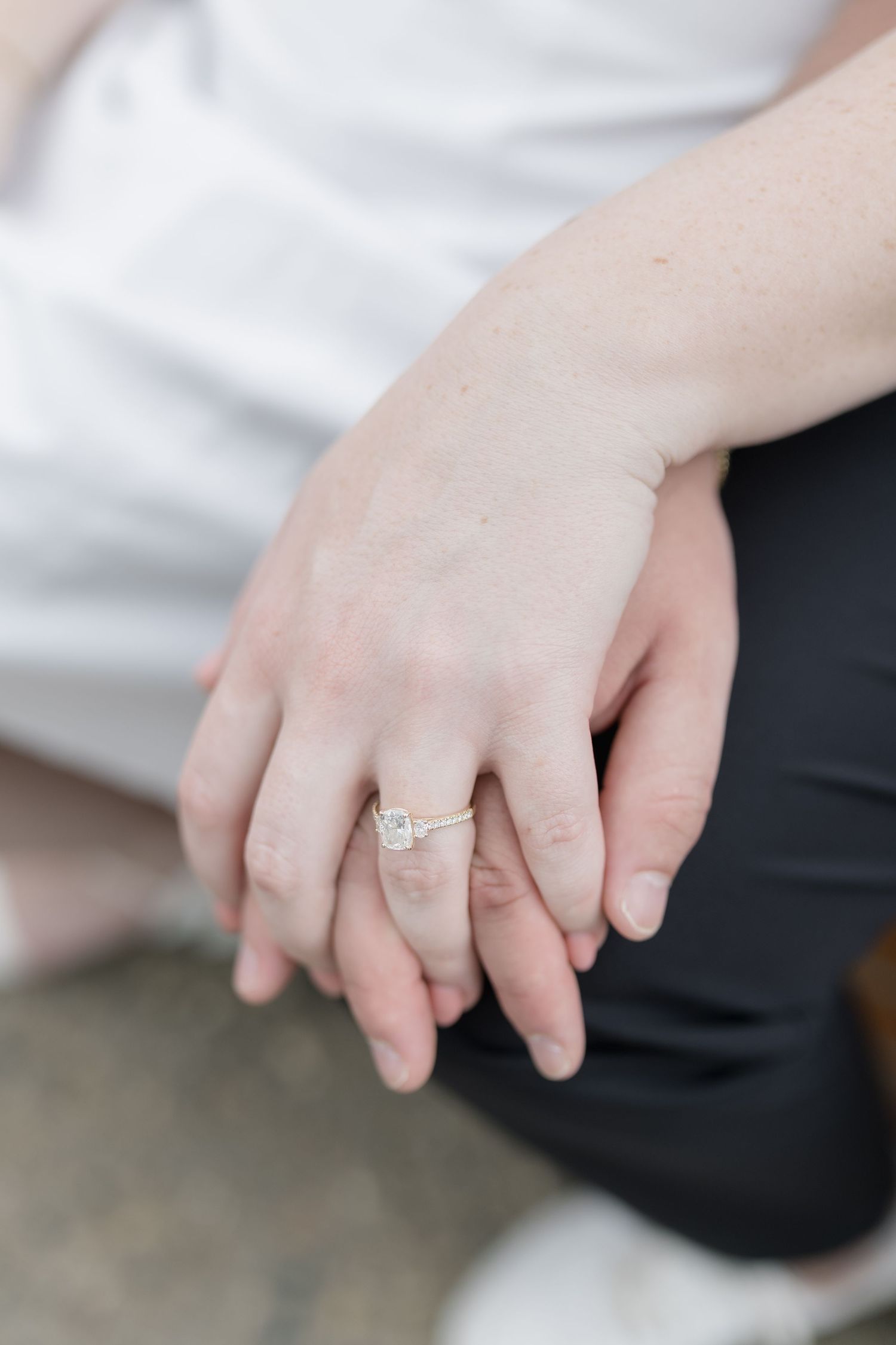 Close-up view of hands wearing an elegant solitaire diamond engagement ring against a light background.