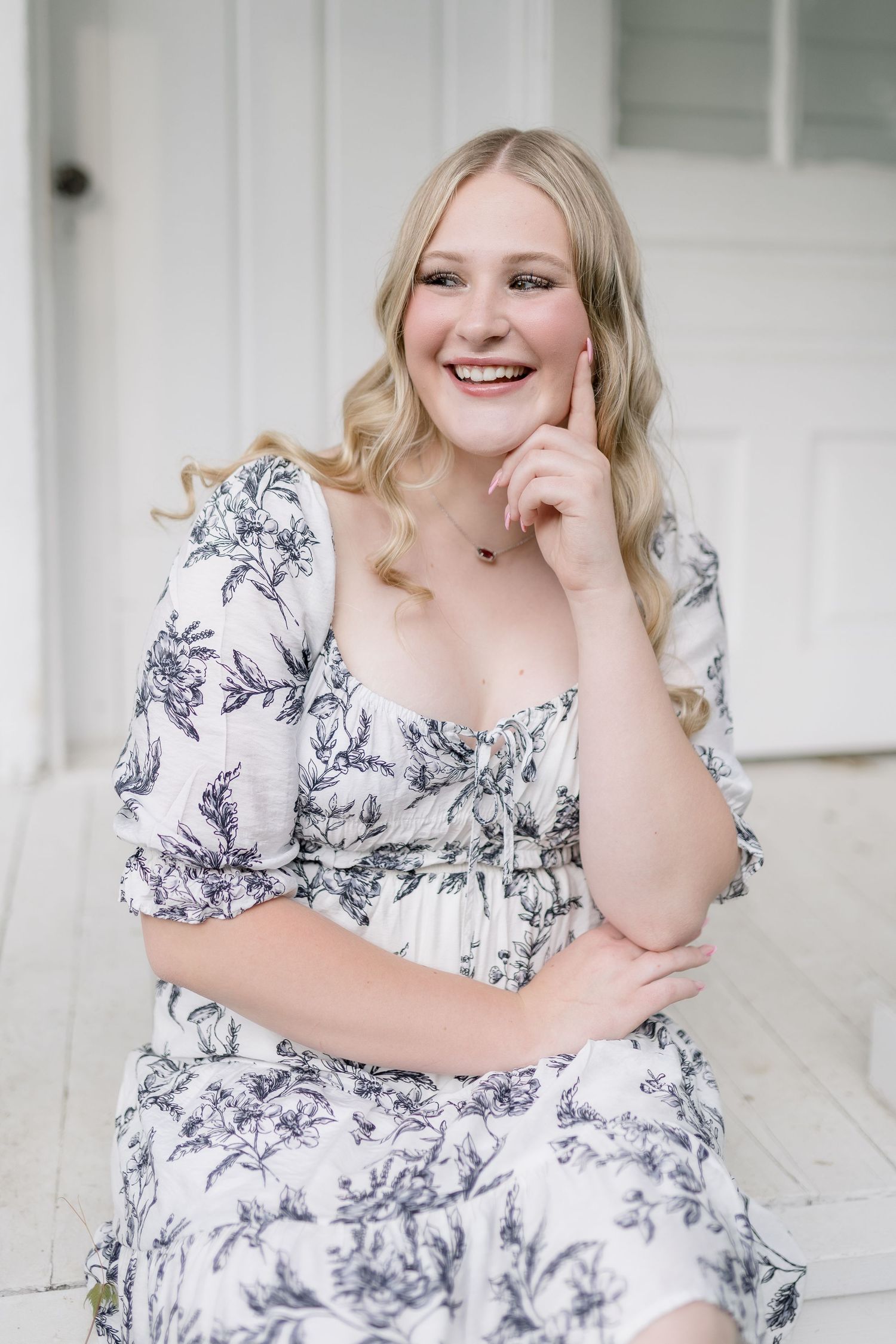 Portrait session on white porch featuring floral dress and joyful expressions.
