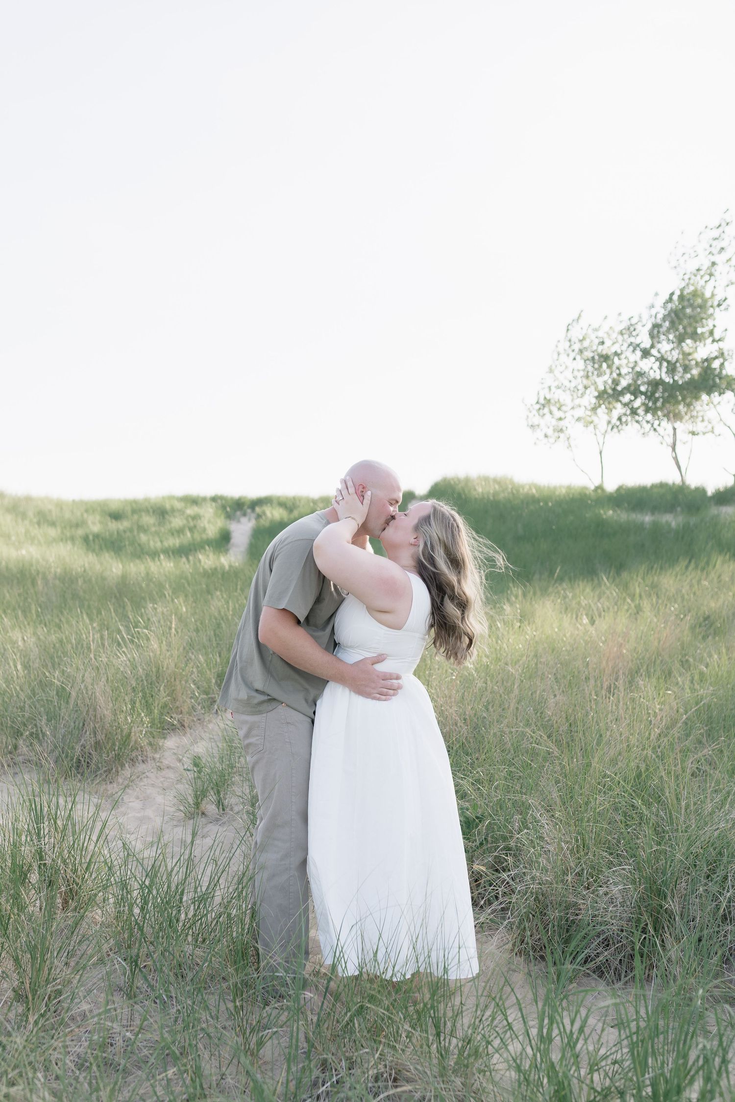 Romantic wedding couple embracing in tall beach grass at sunset.
