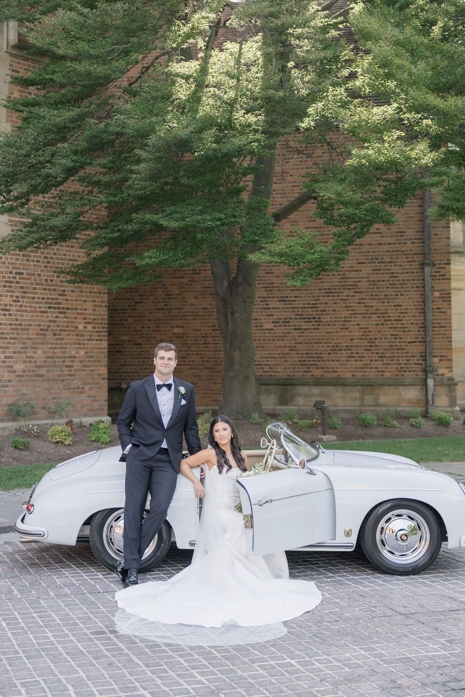 Classic silver vintage car with wedding couple posed against brick wall.
