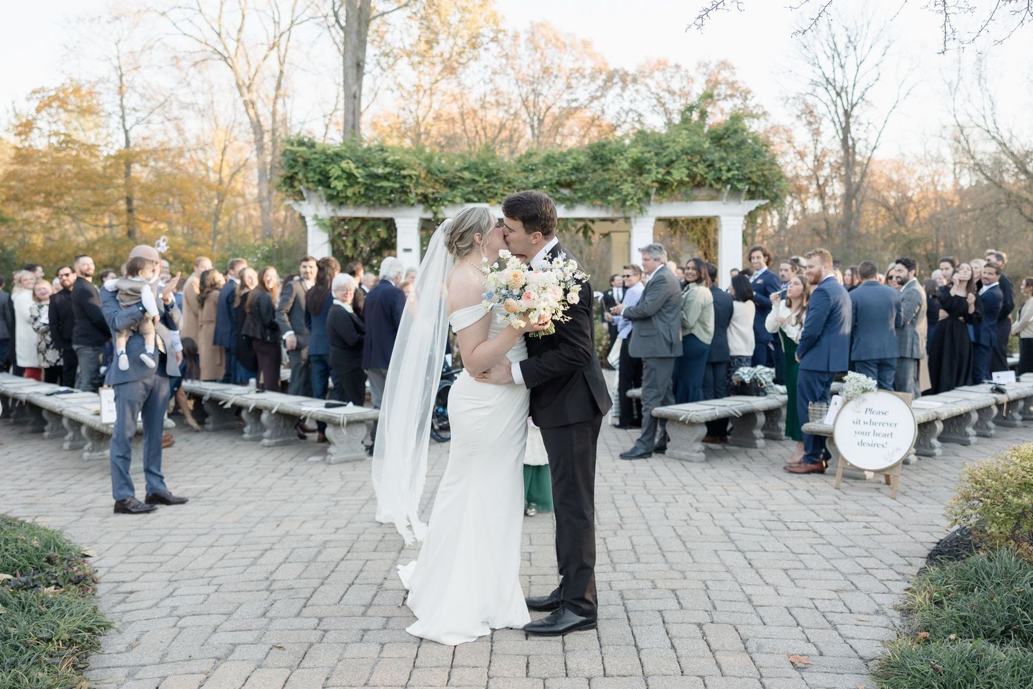 An outdoor wedding ceremony with guests seated on benches watching the celebration.