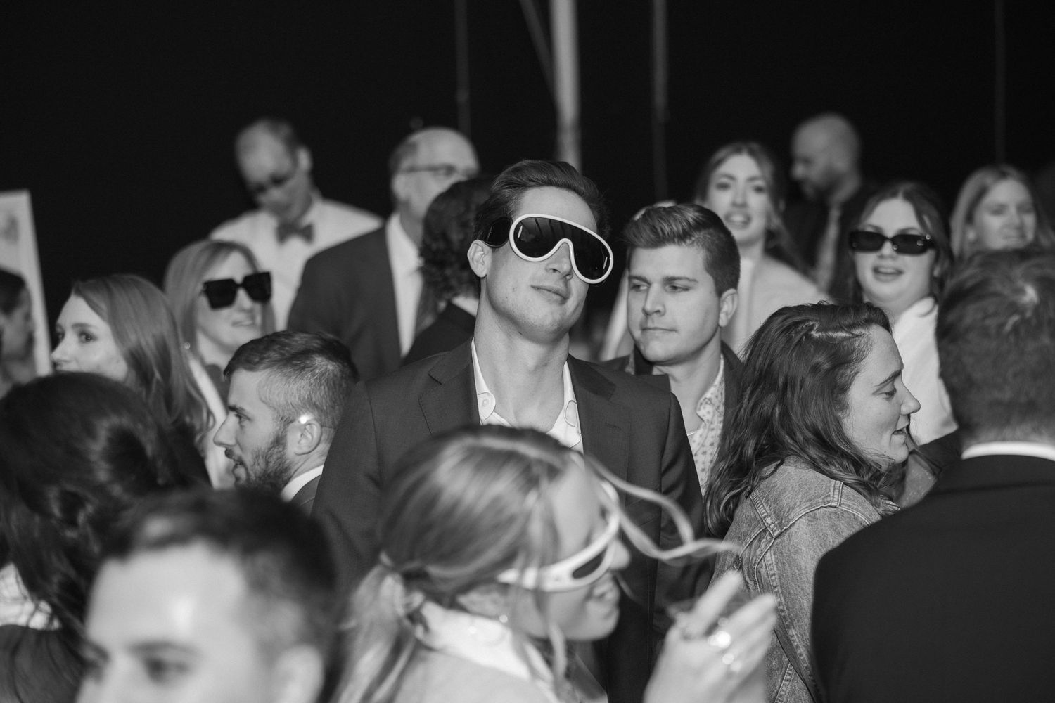Black and white photo of wedding guests wearing sunglasses during reception party.