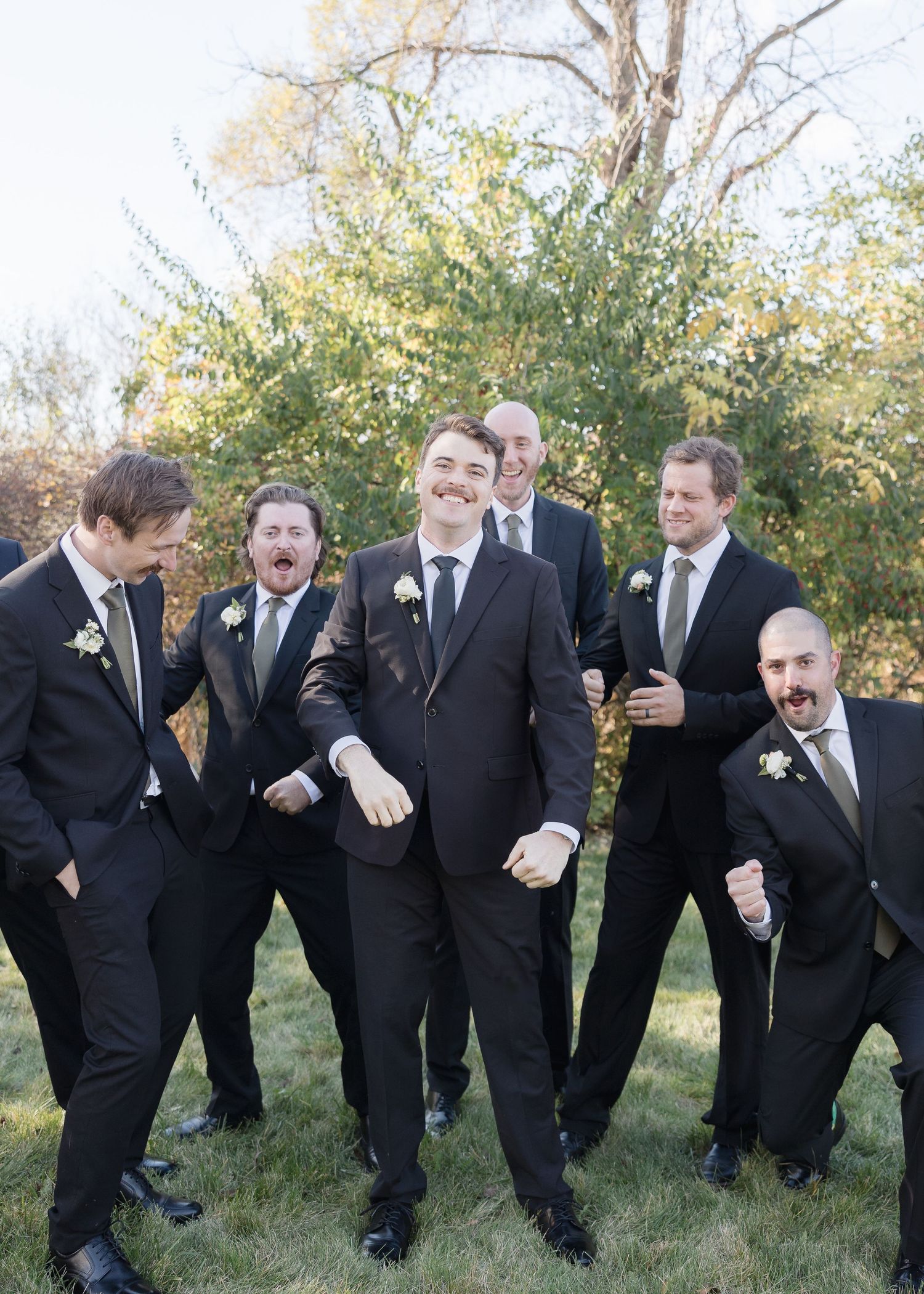 Groomsmen in black suits and ties enjoy lighthearted moment during outdoor photo session.