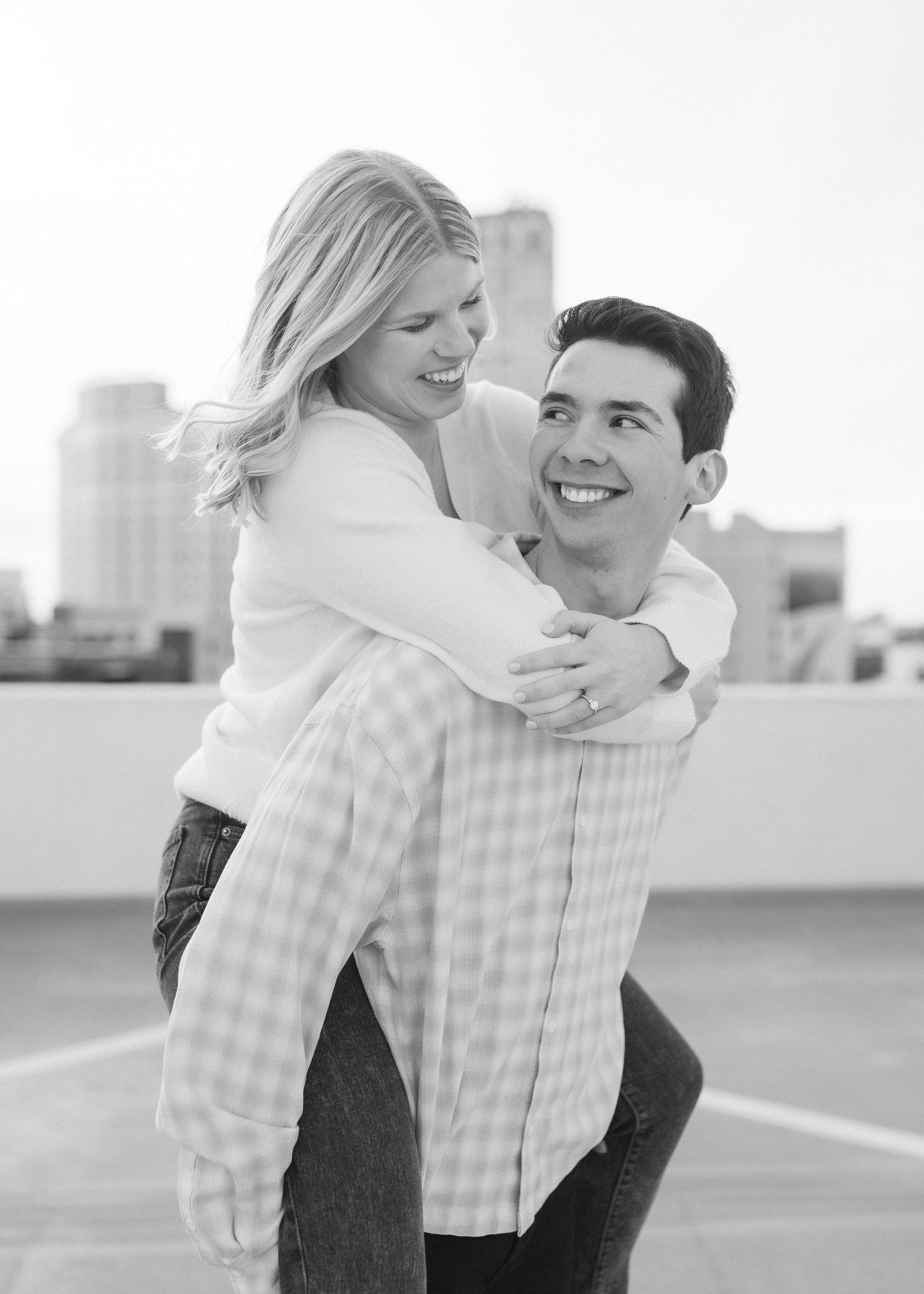 A playful black and white portrait of a couple embracing on an urban rooftop.