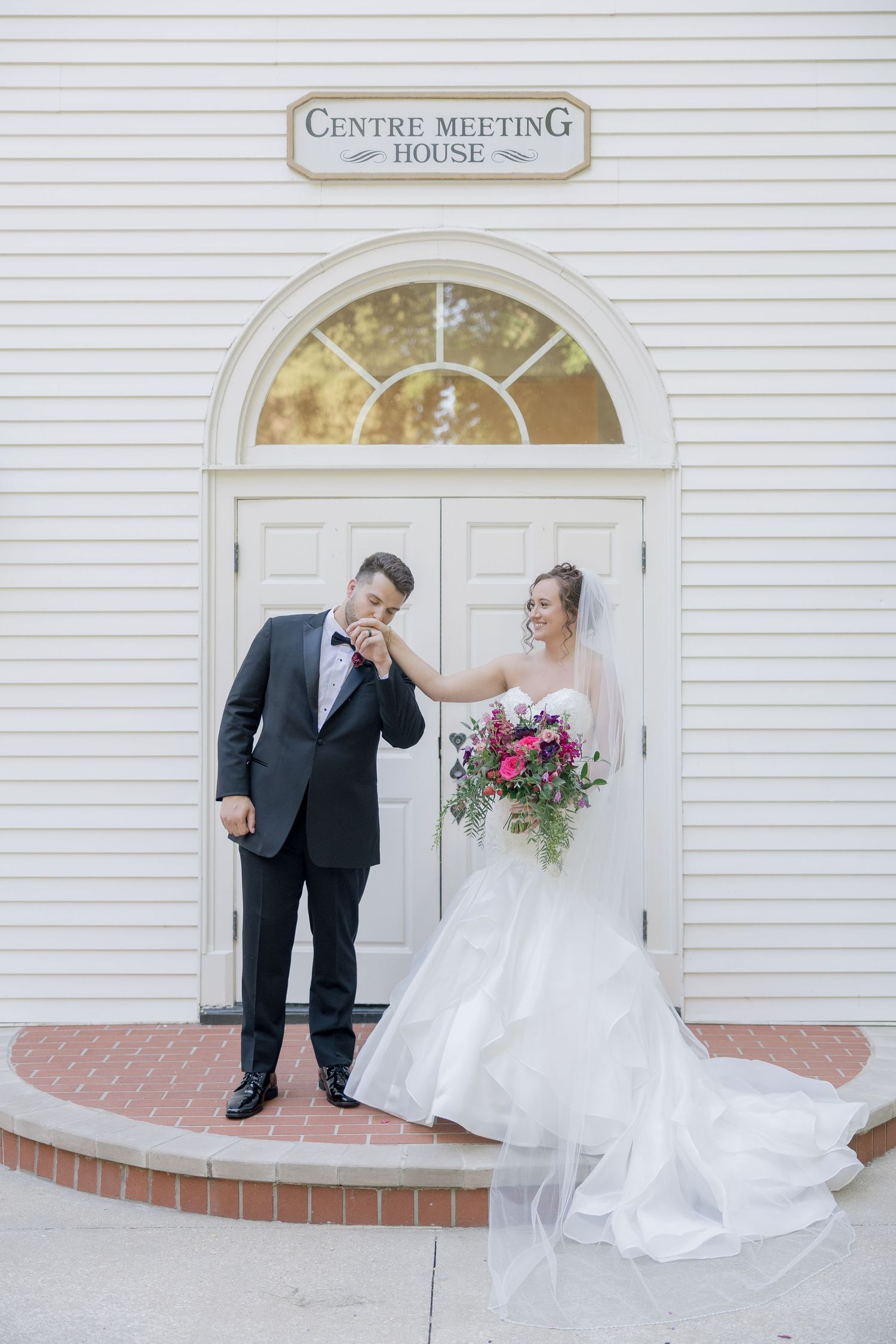 Wedding couple shares a playful moment on the steps of Centre Meeting House with elegant white dress and black suit.