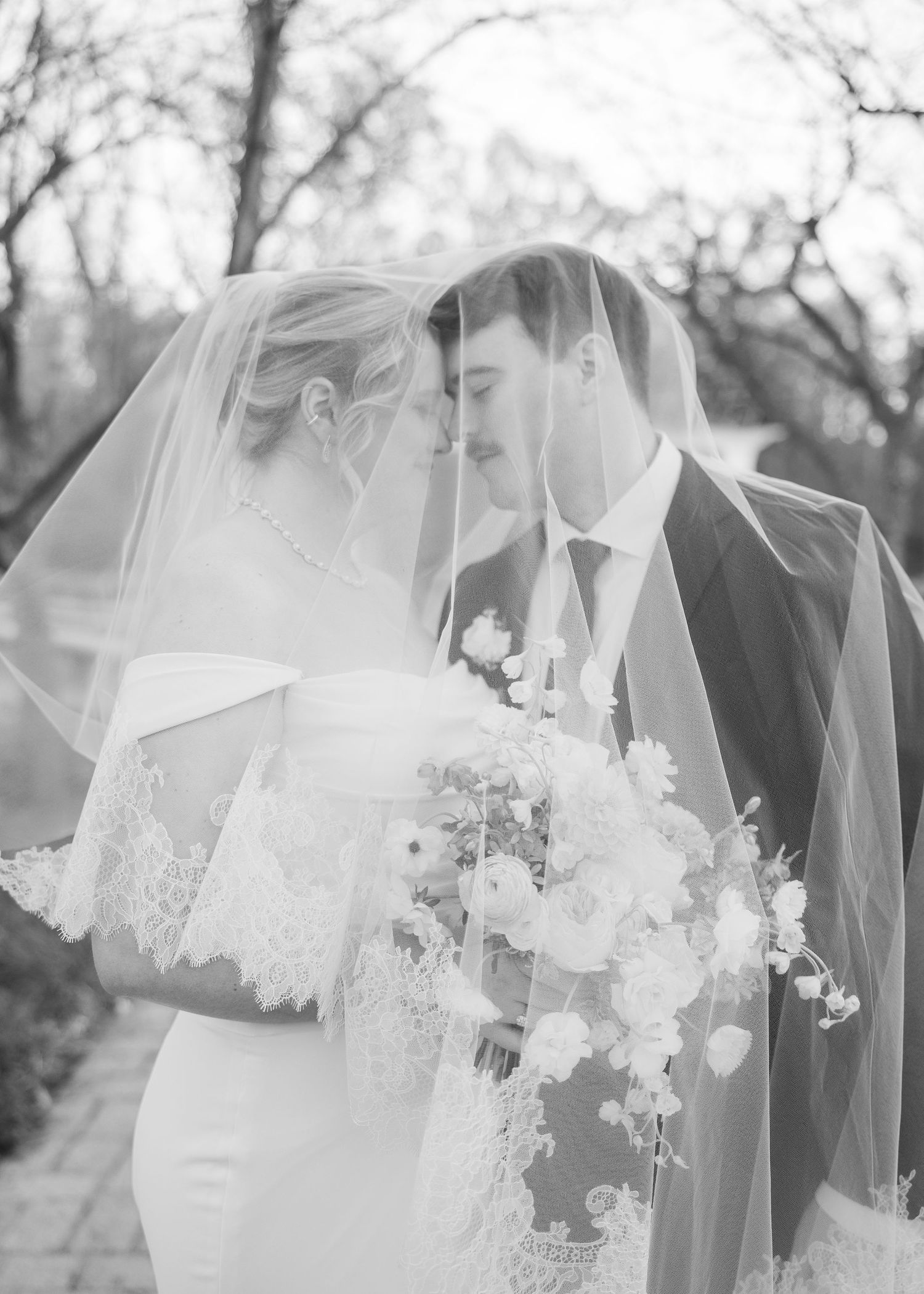 Intimate black and white portrait of couple sharing tender moment under wedding veil.