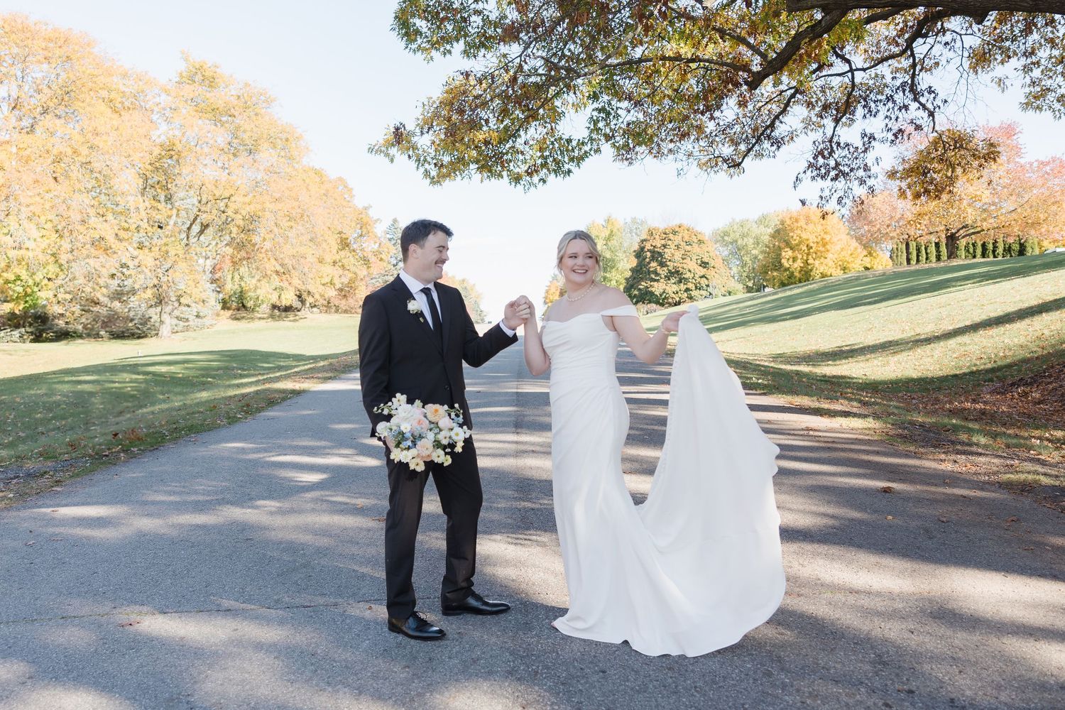 Newlyweds share joyful moment on tree-lined autumn path during outdoor wedding ceremony.