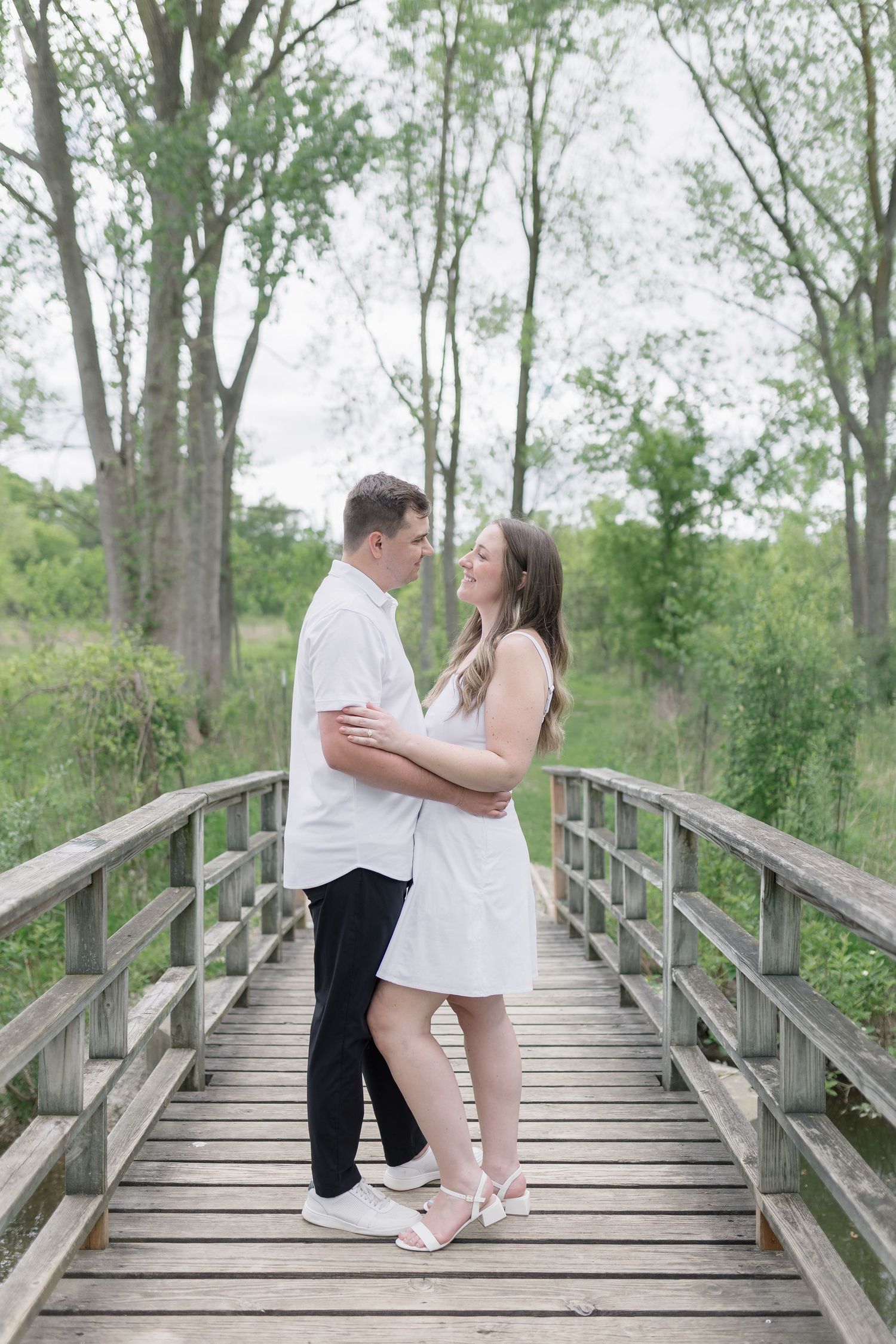 A romantic couple shares tender moments on a wooden boardwalk surrounded by lush green trees in a natural setting.