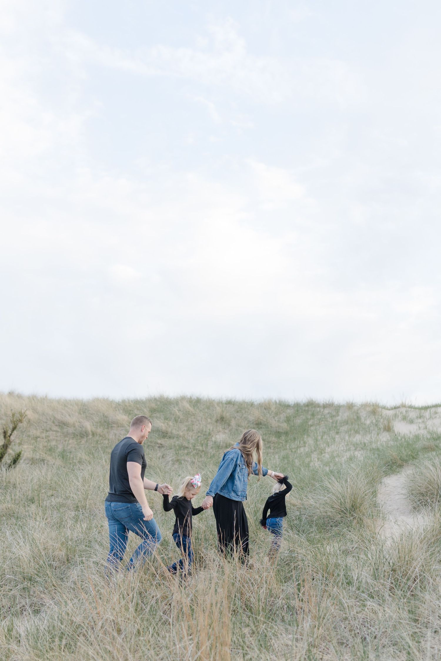 Family walking together through tall grass in sand dunes on an overcast day with their dogs.