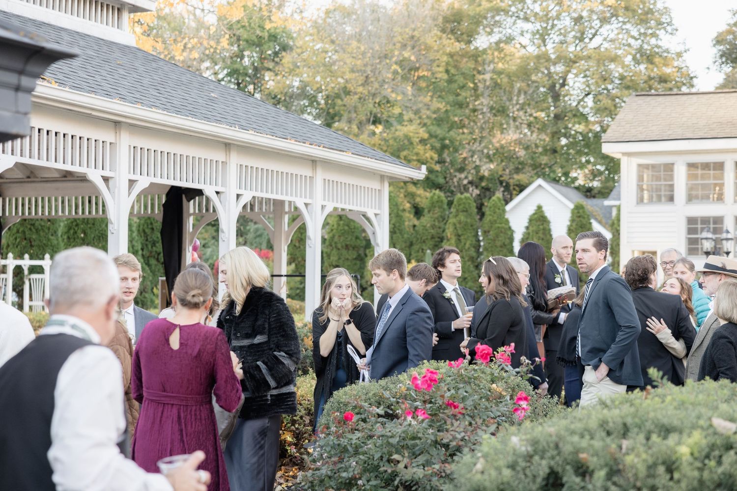 Wedding guests mingling outside a white building with a covered porch.
