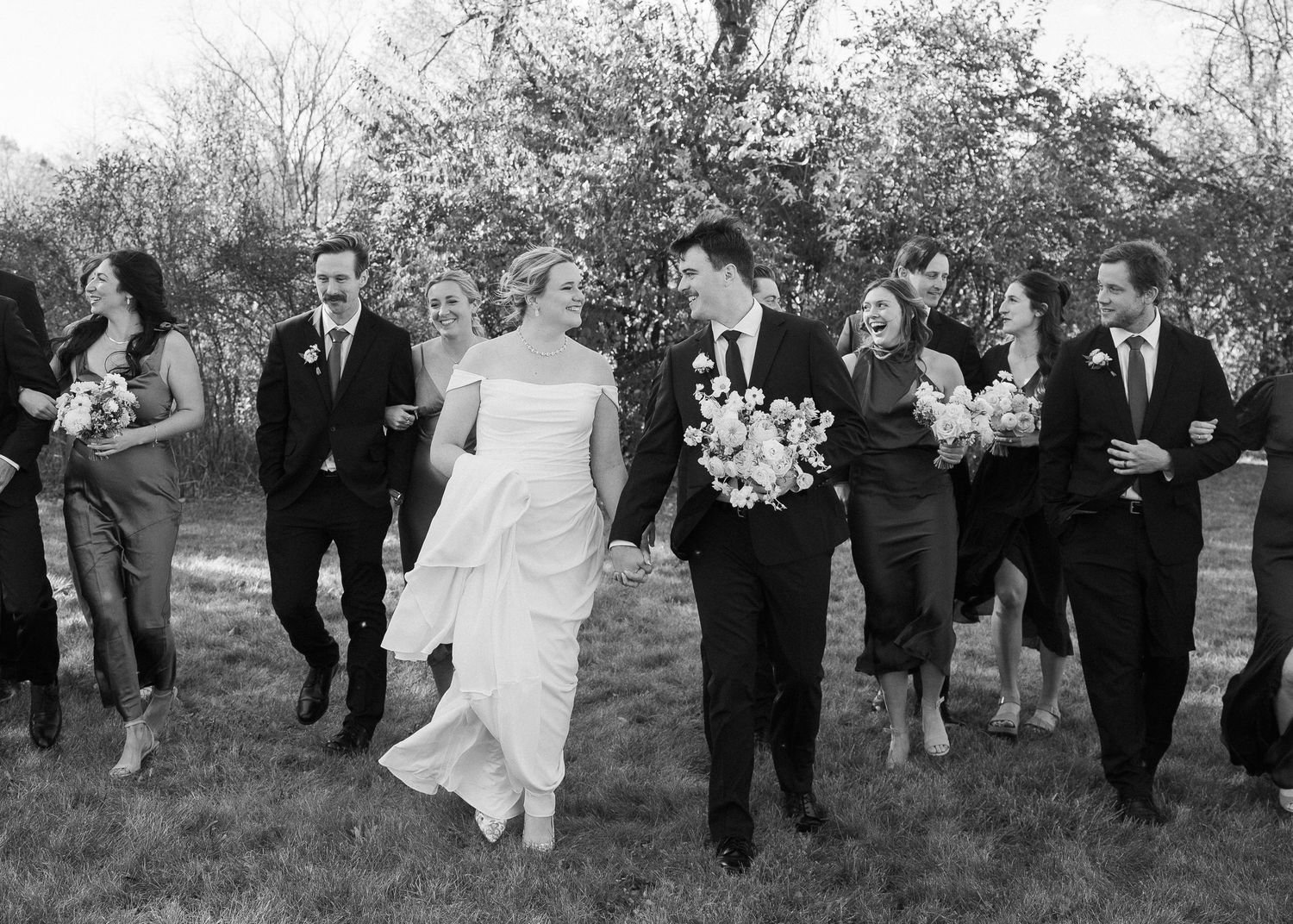 A wedding party walks together outdoors while carrying bouquets in this black and white photograph.