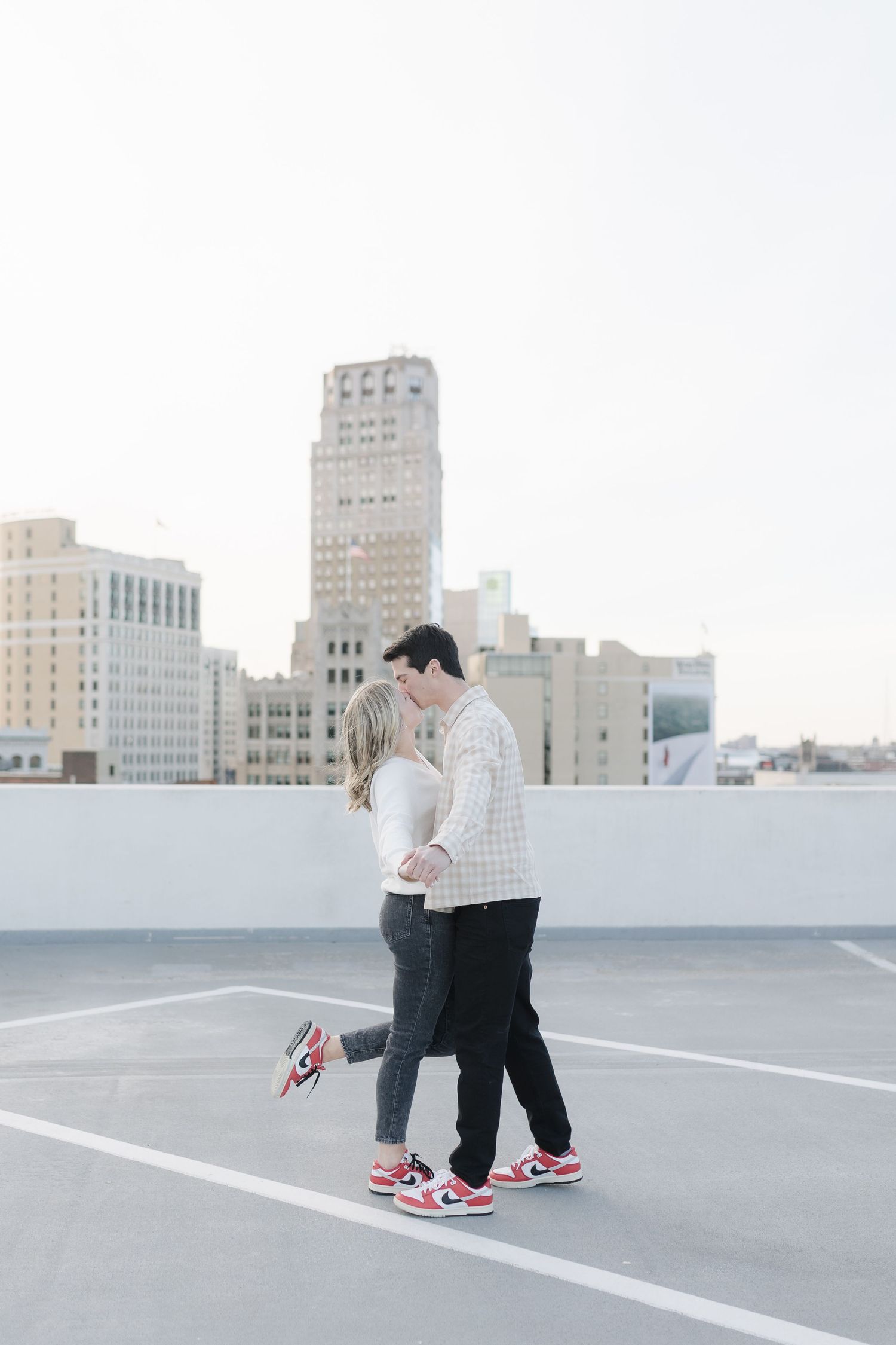 A sweet encounter between two people wearing matching sneakers on a rooftop with an urban skyline backdrop.