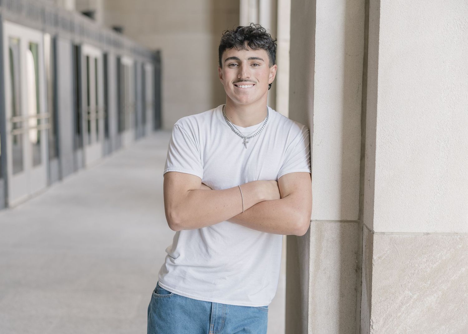 Person in white t-shirt and jeans poses against light colored building columns in outdoor setting.
