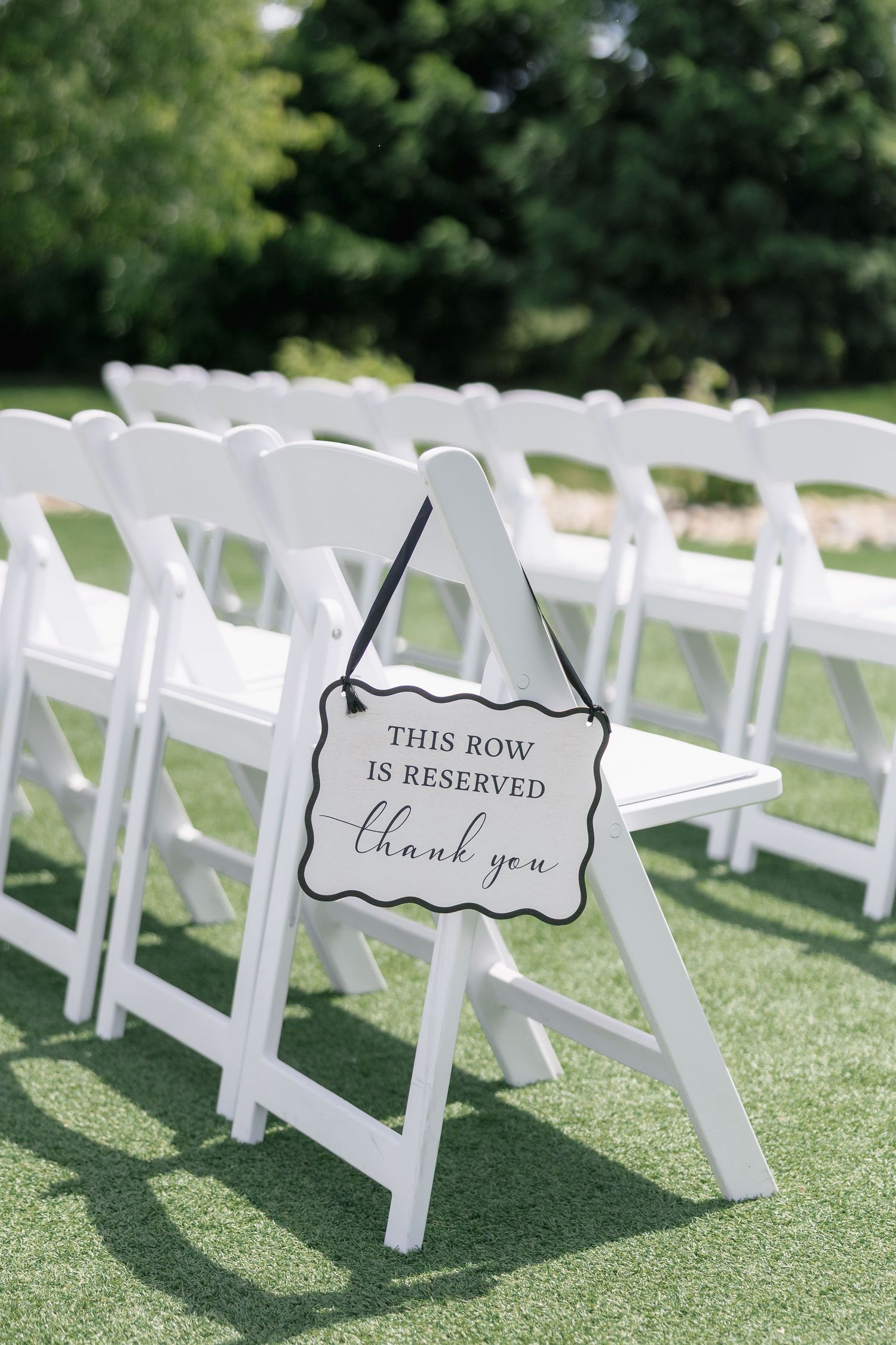 White folding chairs with reserved row sign at outdoor wedding ceremony on green grass.
