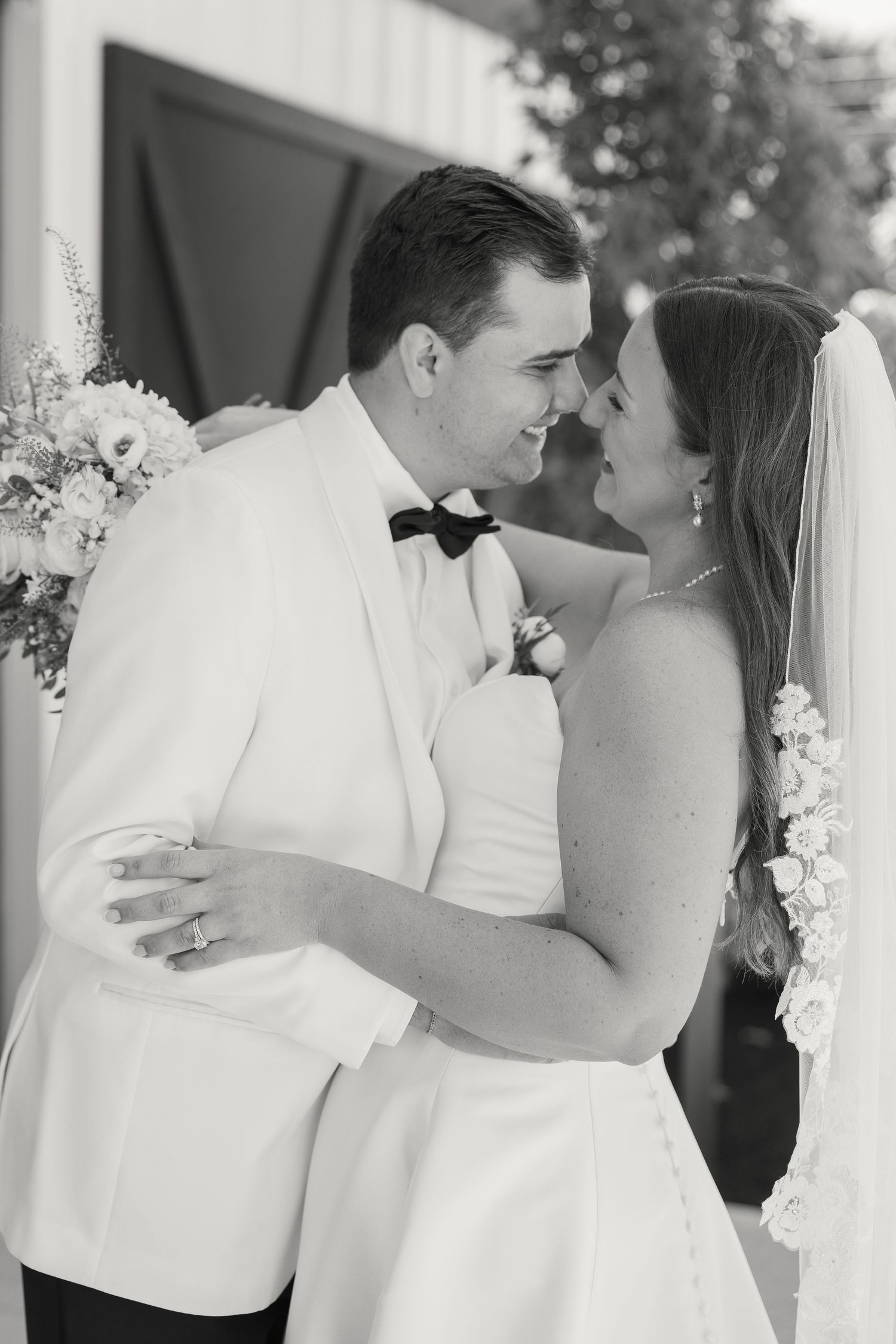 Black and white photo of a bride and groom embracing and smiling at each other on their wedding day.