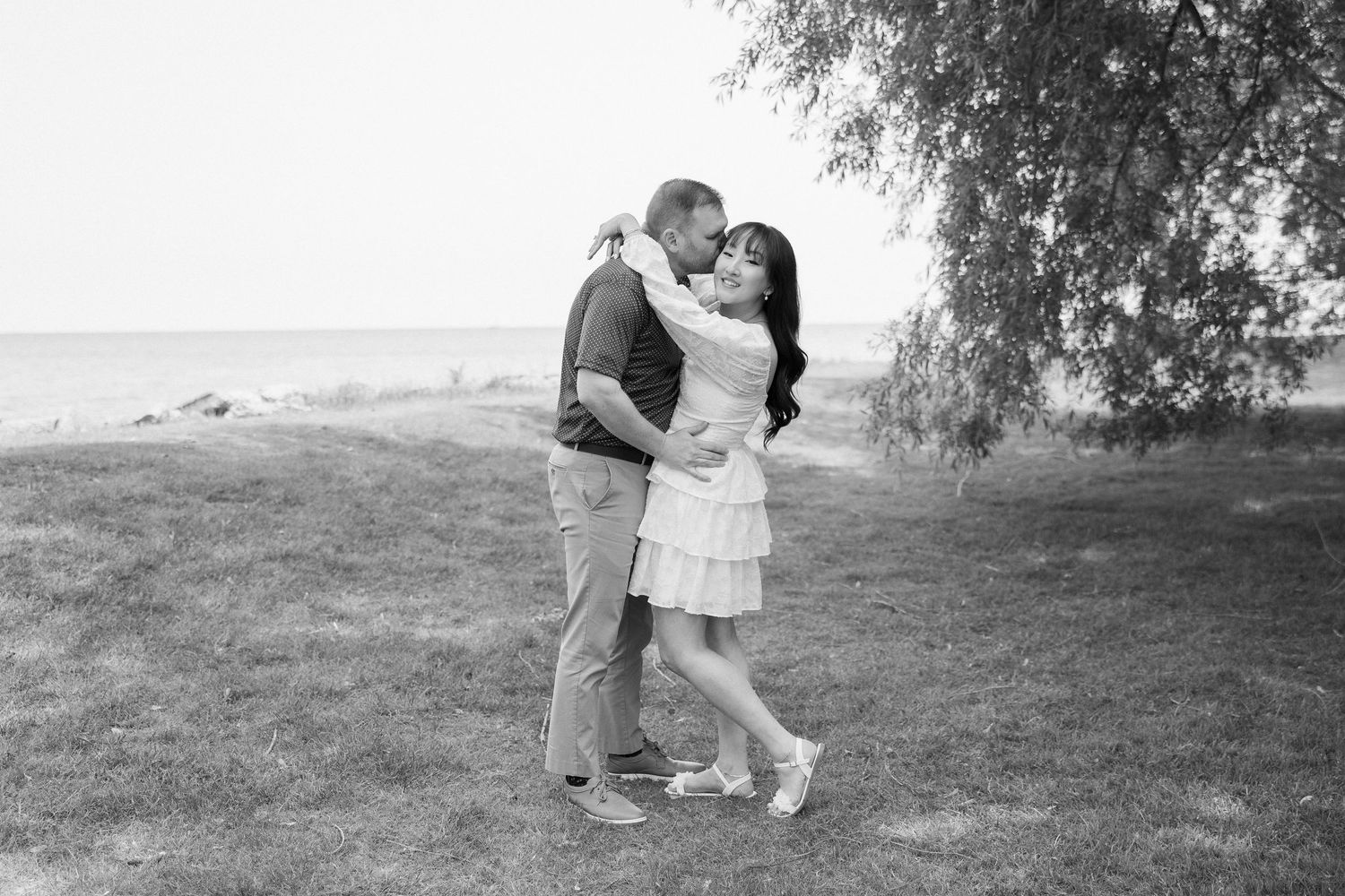 A couple shares an intimate moment on a grassy hillside during a romantic outdoor photoshoot.