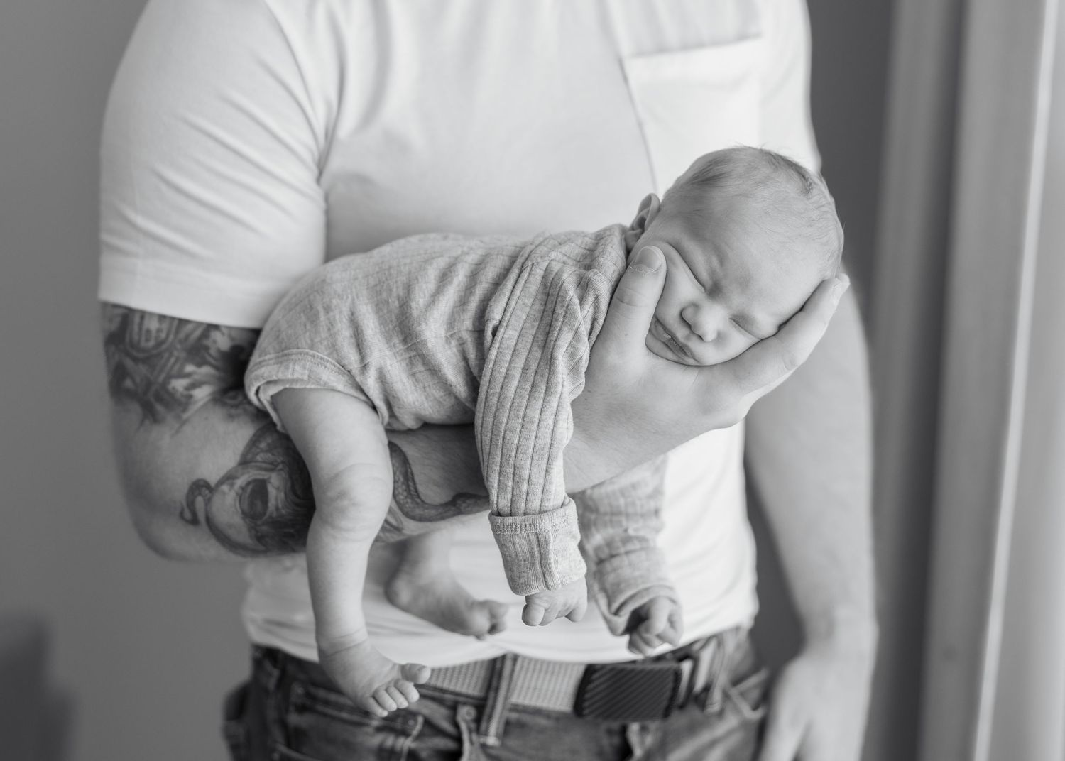A person wearing a white t-shirt and jeans holds a small gray kitten close to their chest.